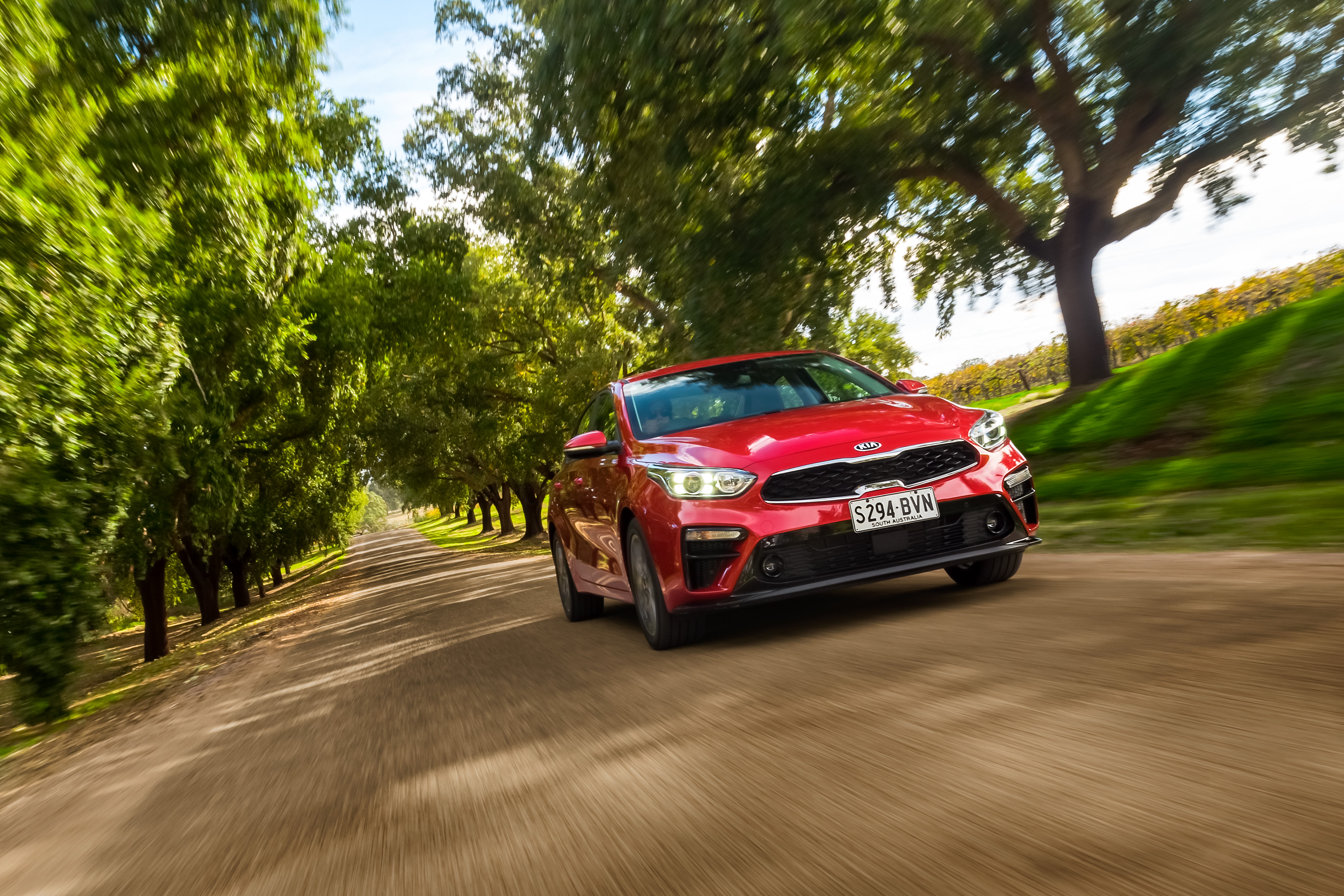 Red Kia Cerato Sport Plus driving on a scenic tree-lined road HD Wallpaper