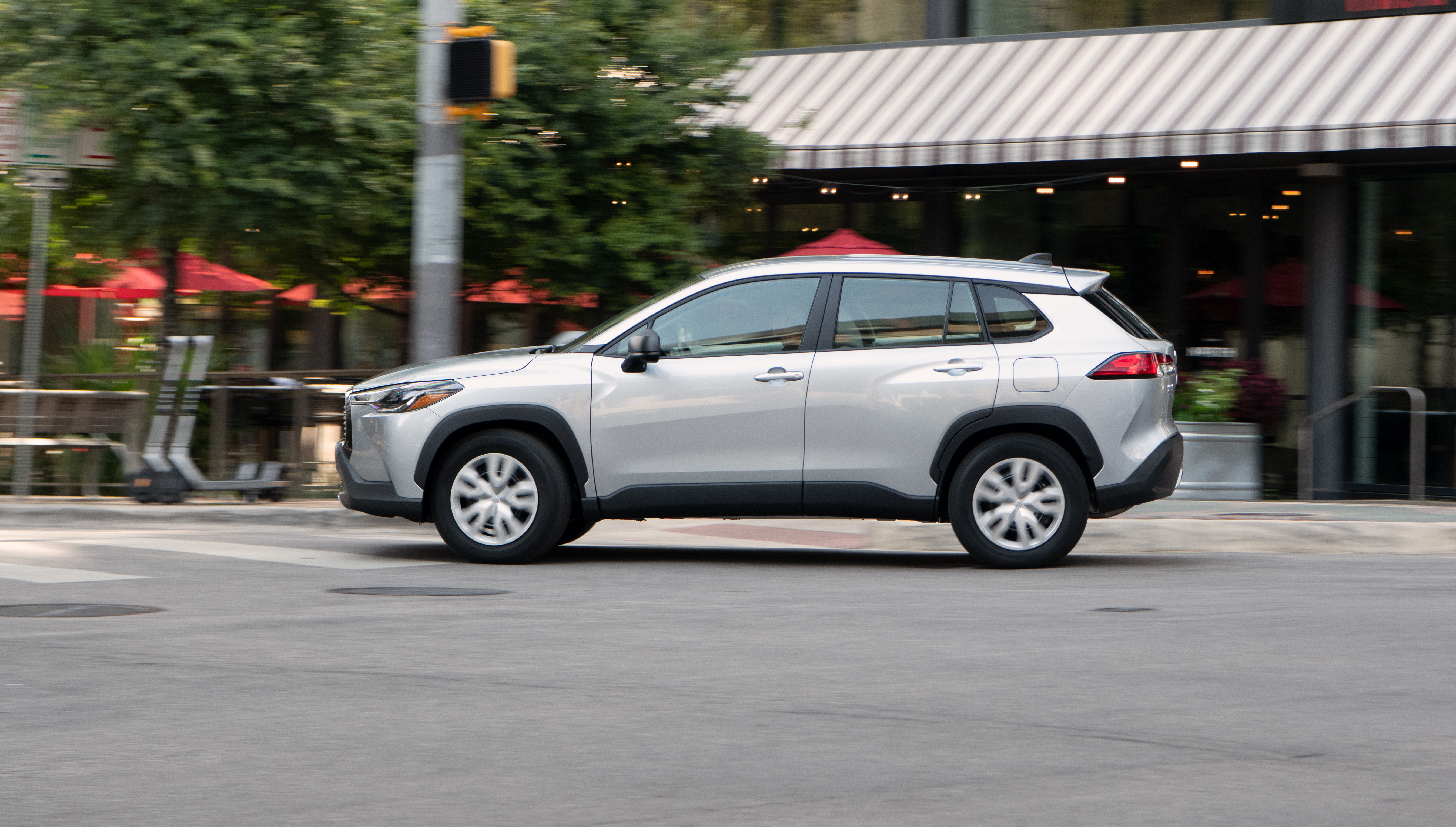 Silver Toyota Corolla Cross SUV driving on city street HD Wallpaper