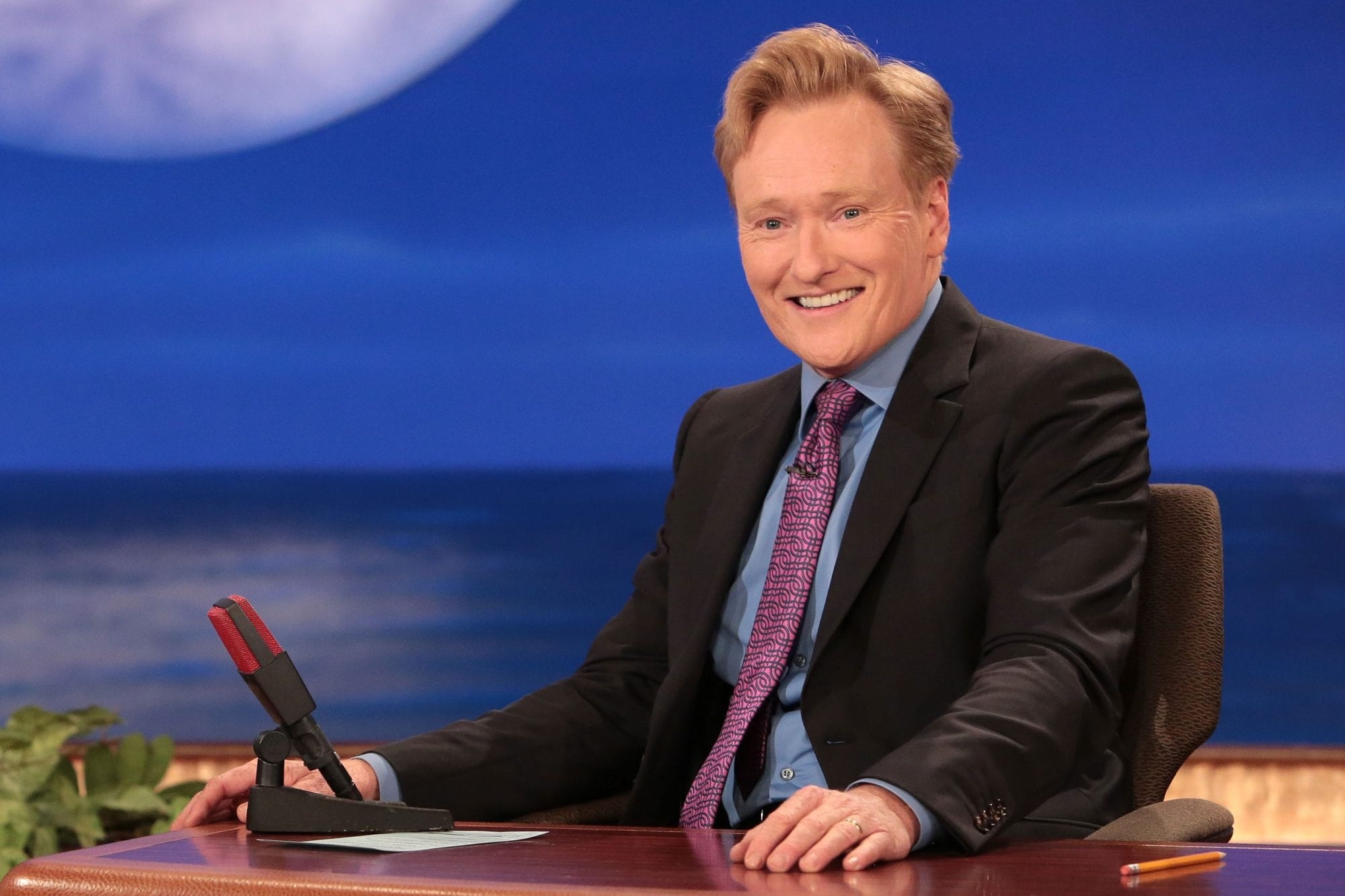 Conan O'Brien smiling at his desk HD Wallpaper