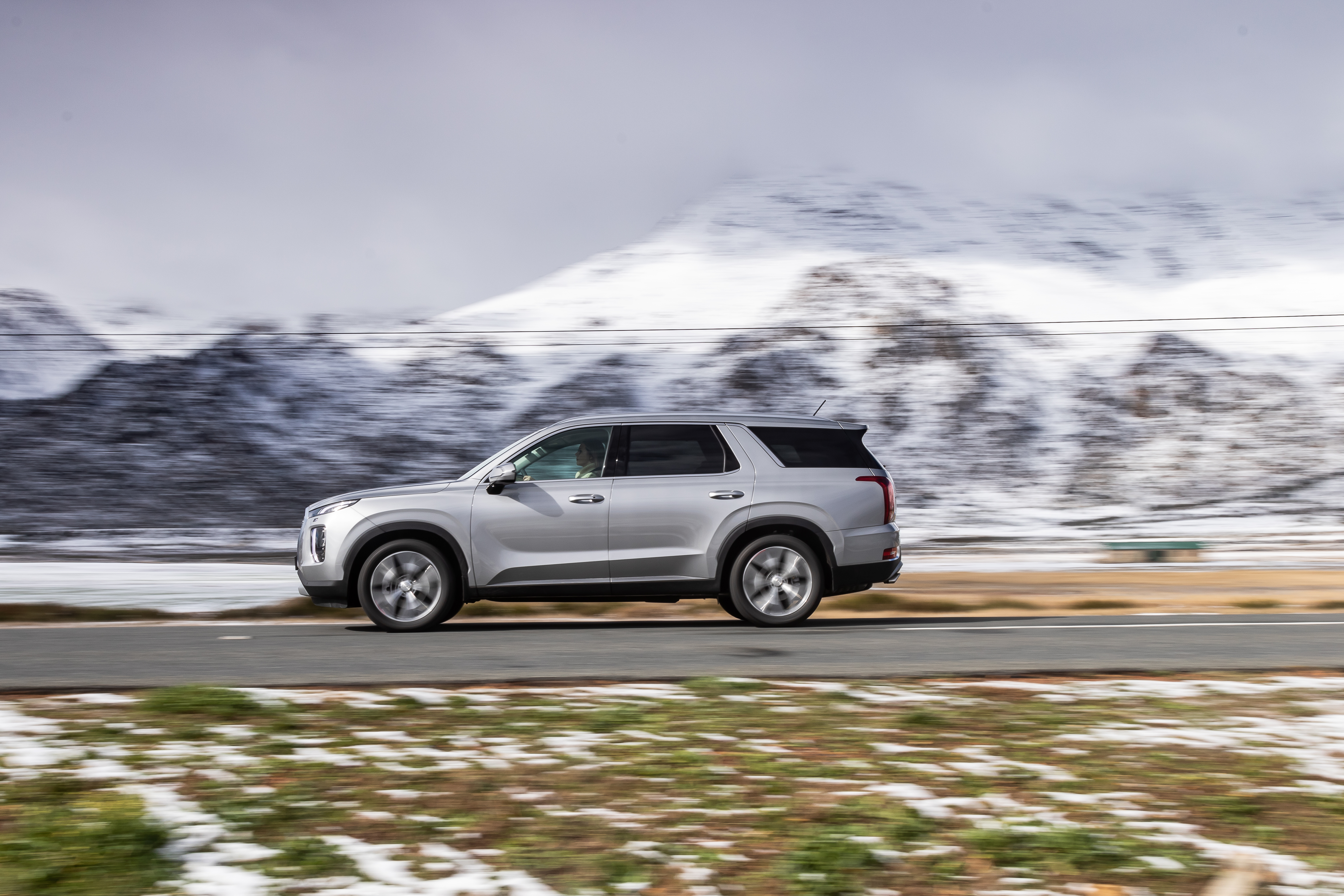 Hyundai Palisade SUV driving through snowy mountains HD Wallpaper