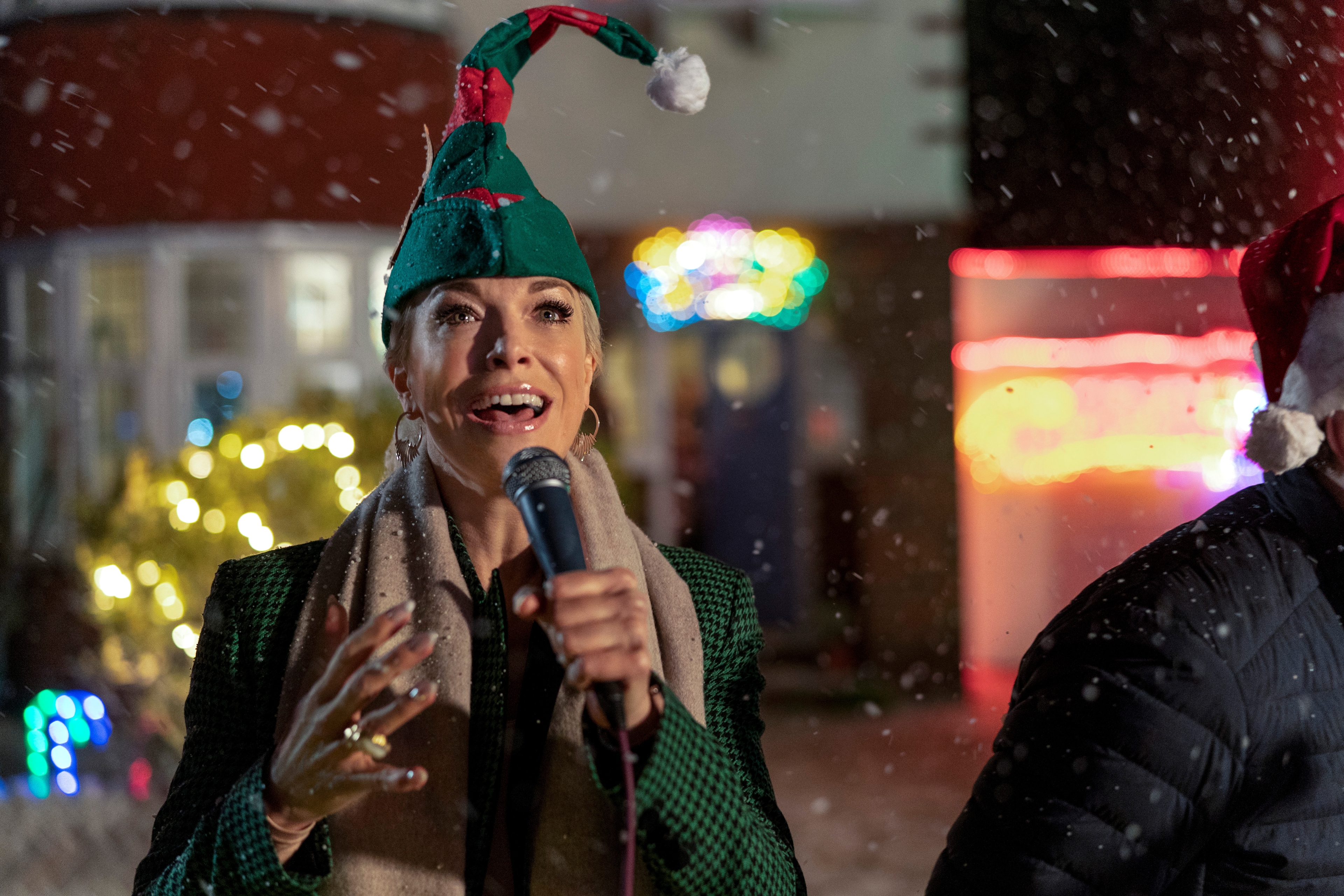 Hannah Waddingham in elf hat singing during snowy Christmas HD Wallpaper