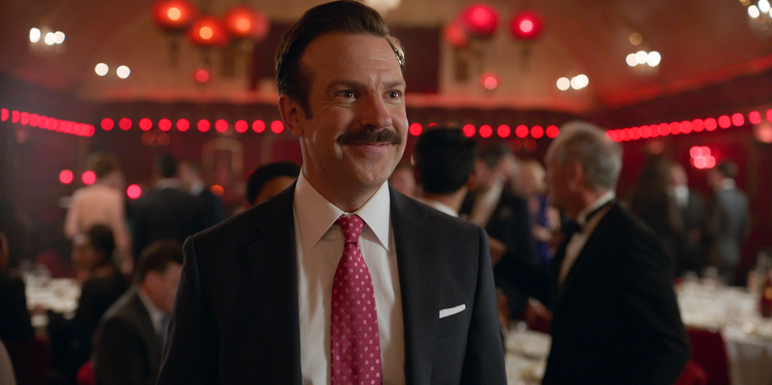 Ted Lasso smiling in a suit at a red-lit party HD Wallpaper