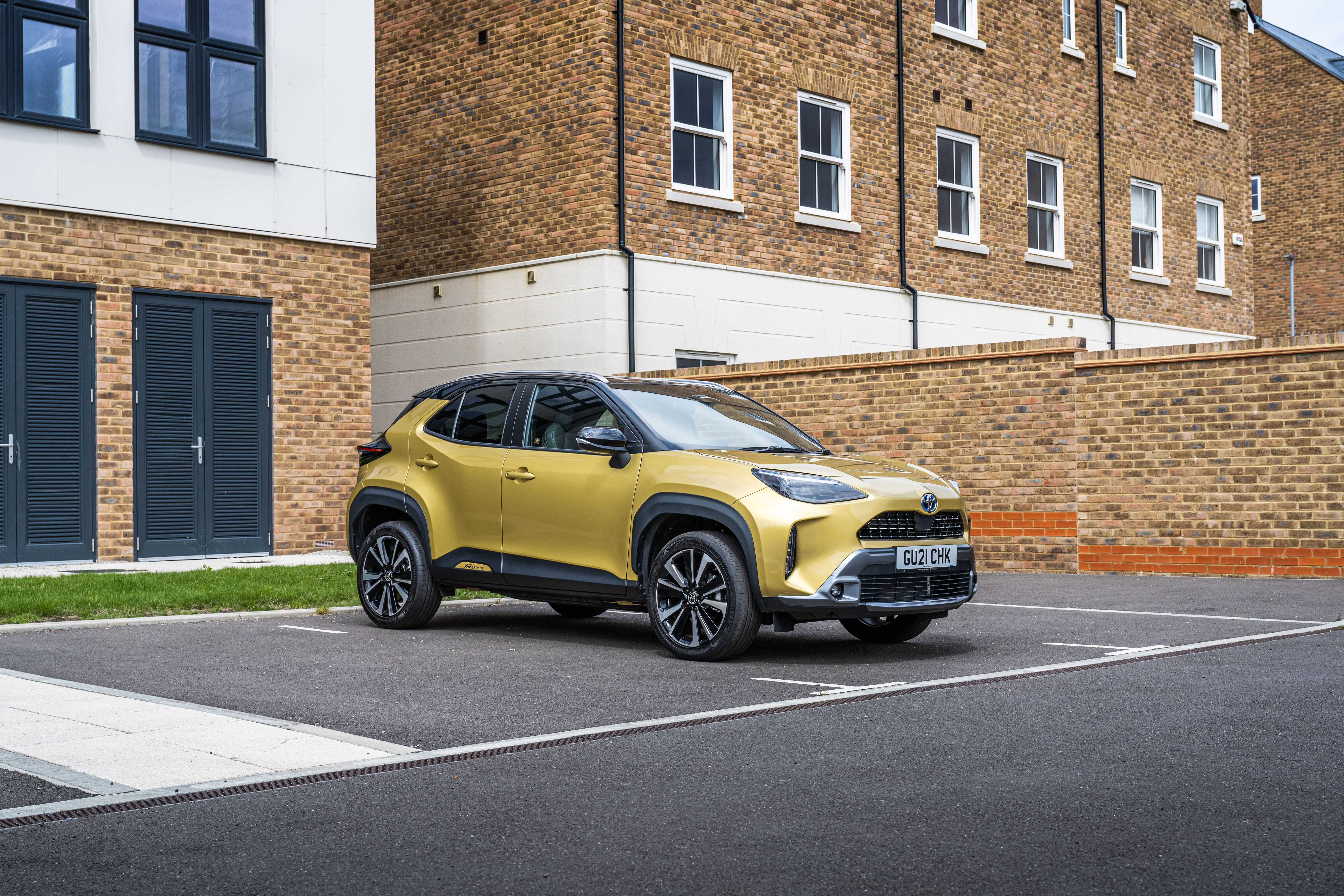 Gold Toyota Yaris Cross Hybrid SUV parked by brick buildings HD Wallpaper