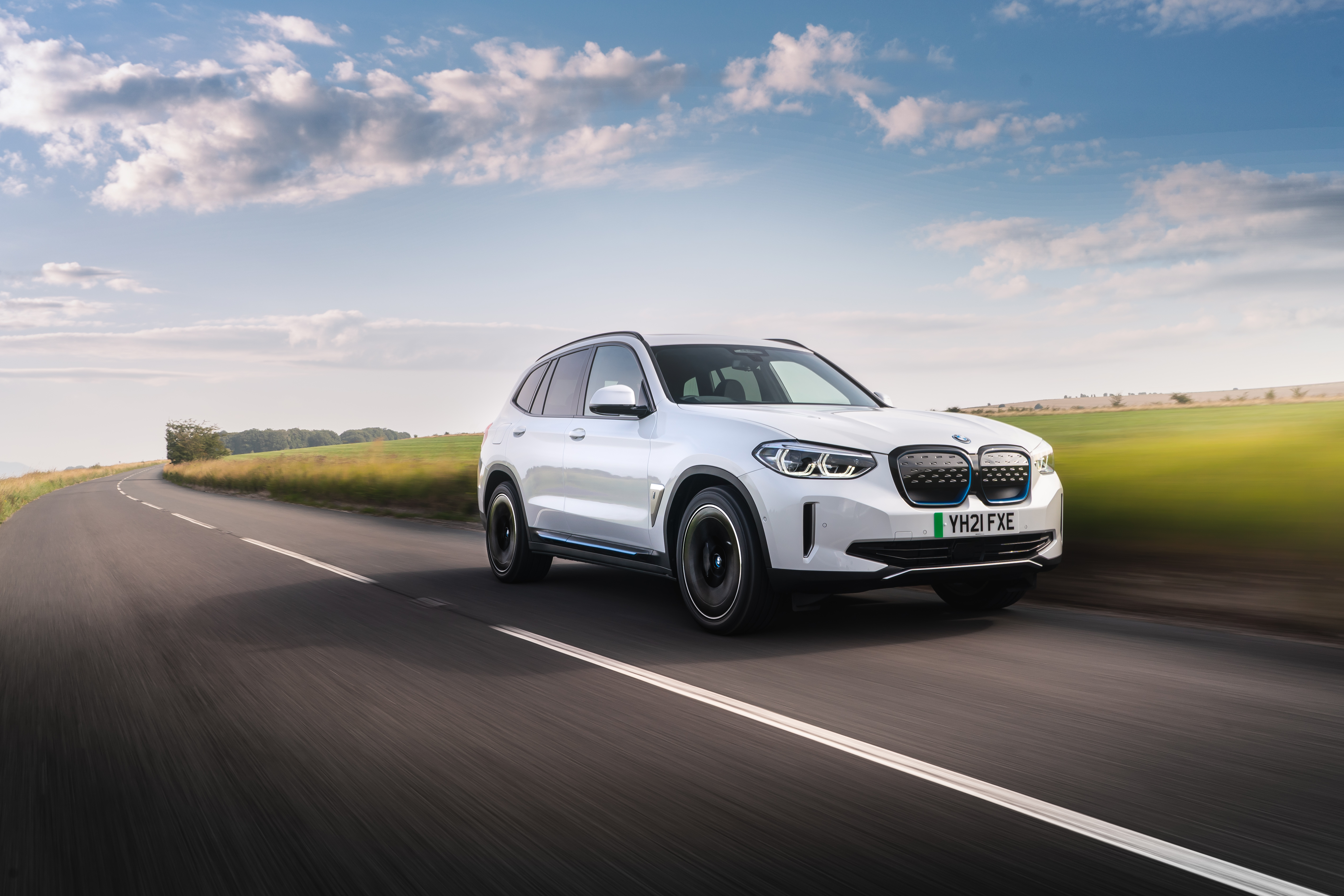 White BMW iX3 Electric SUV driving on a scenic road HD Wallpaper