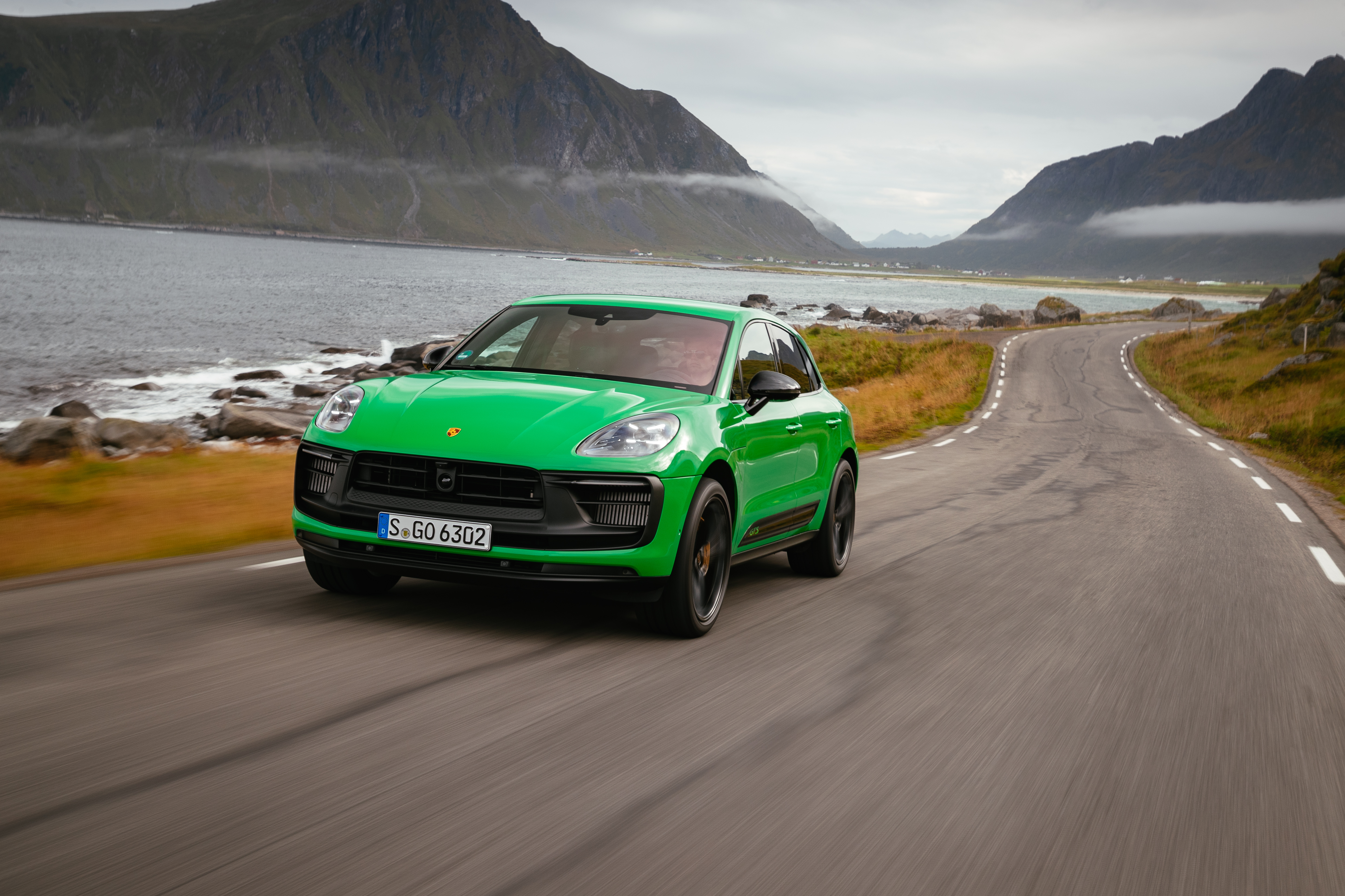 Green Porsche Macan GTS on a scenic coastal road HD Wallpaper