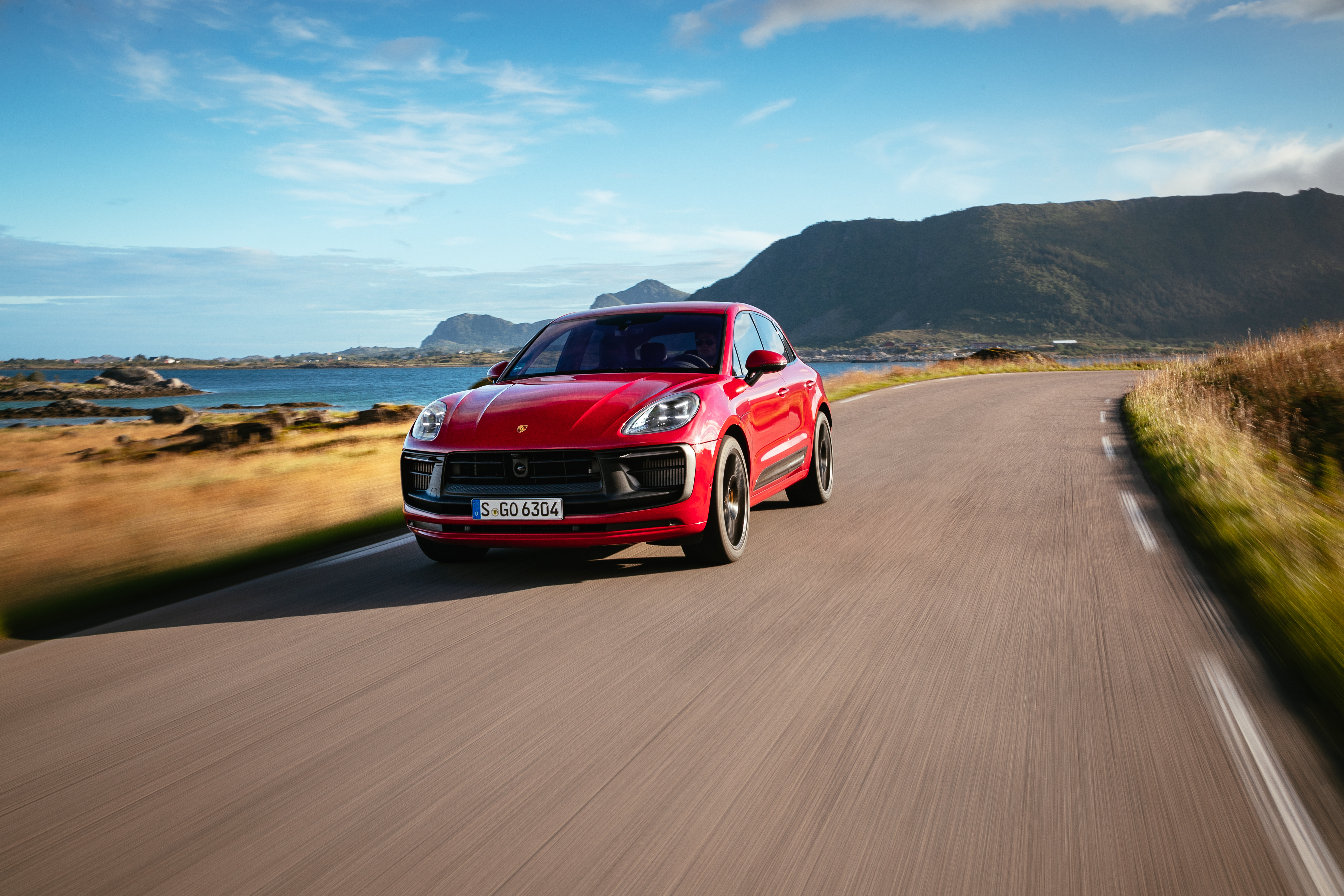 Red Porsche Macan GTS on a scenic coastal road HD Wallpaper