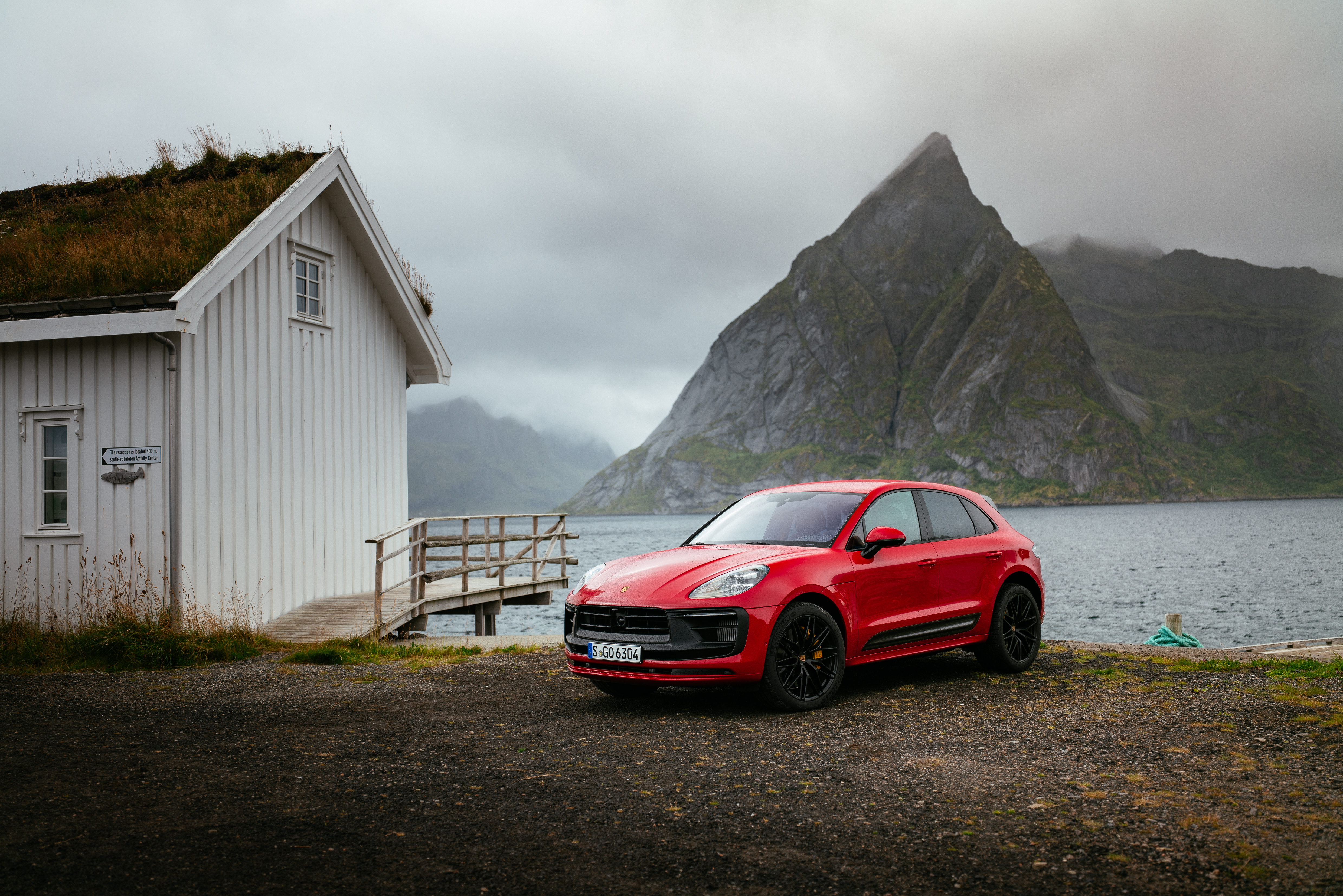 Red Porsche Macan GTS by a grass-roofed house and fjord HD Wallpaper