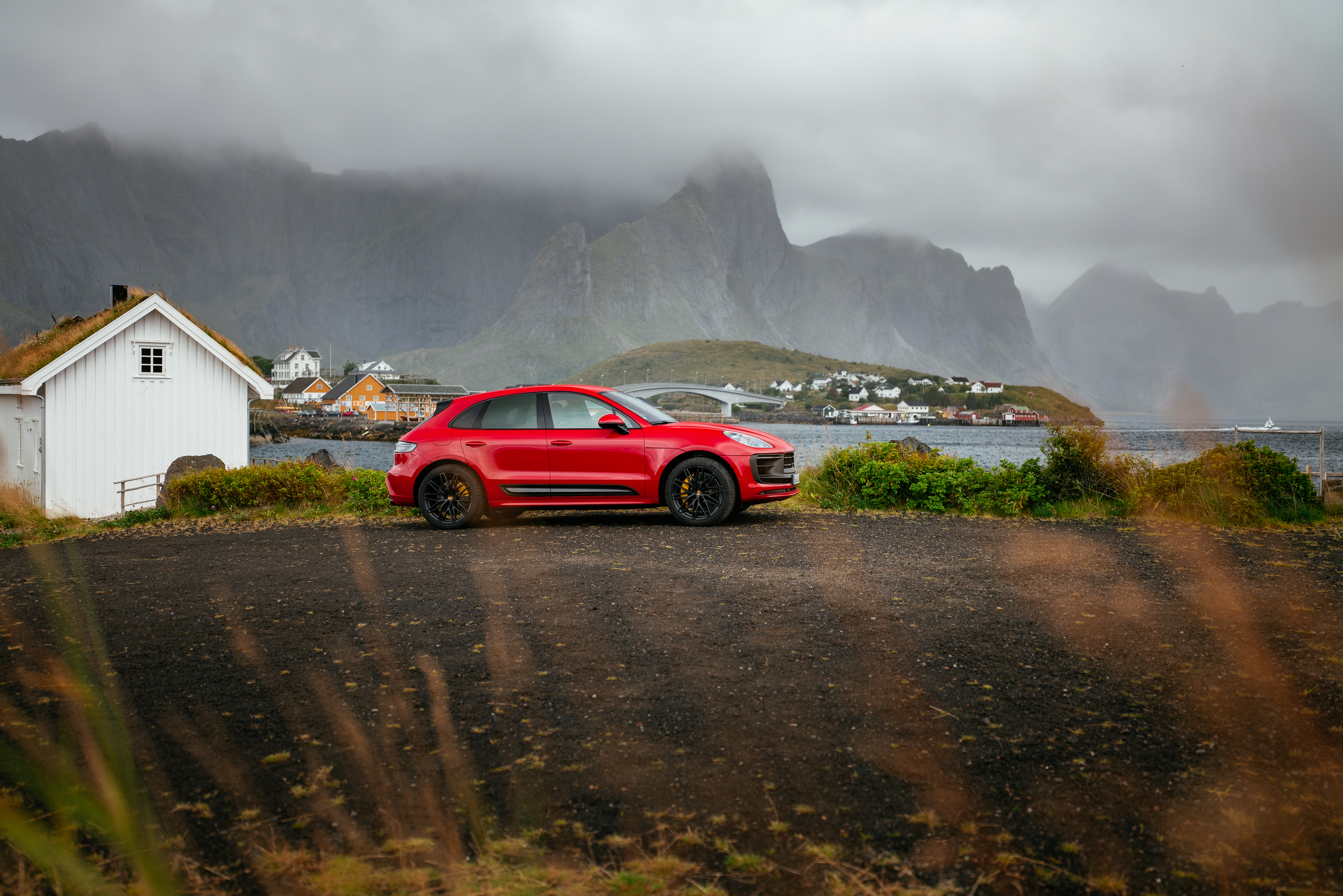 Red Porsche Macan GTS in a scenic cloudy mountain village HD Wallpaper