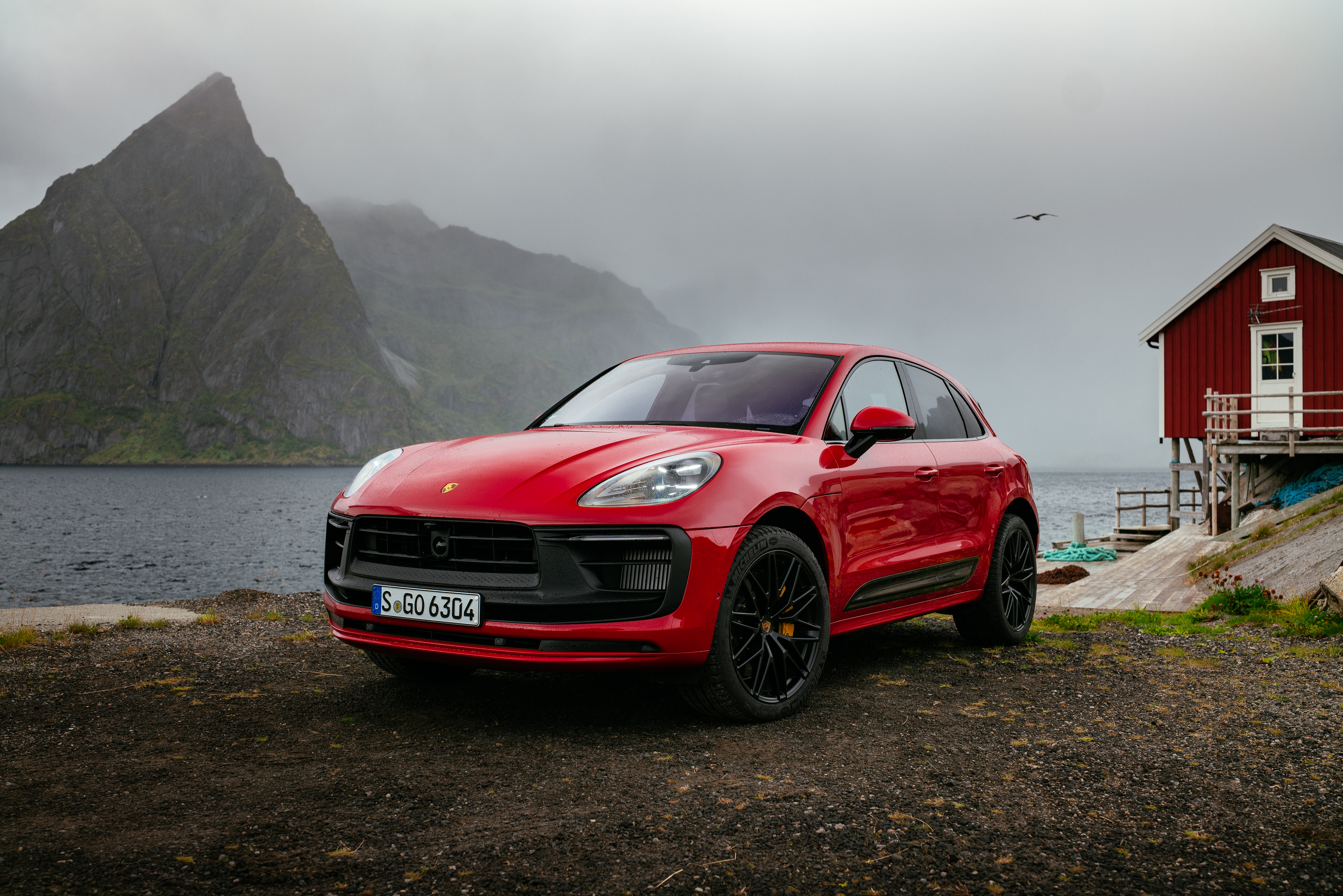 Red Porsche Macan GTS SUV with mountains and red house HD Wallpaper