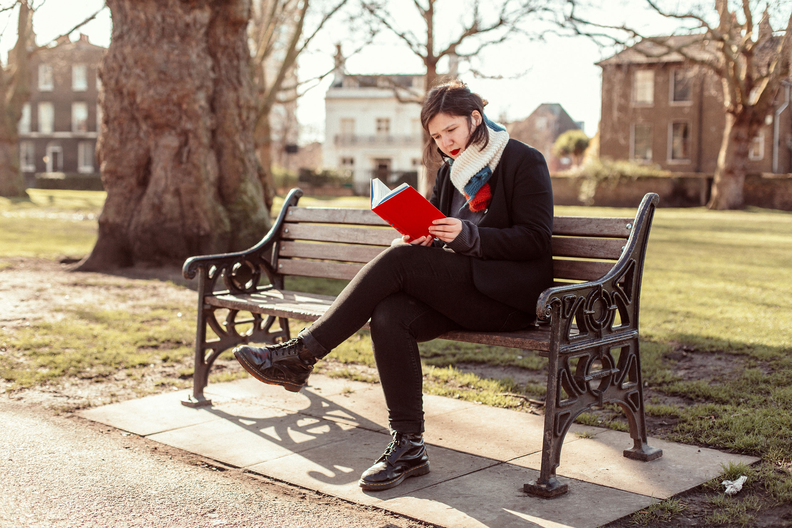 Lucy Dacus reading a red book on a park bench HD Wallpaper