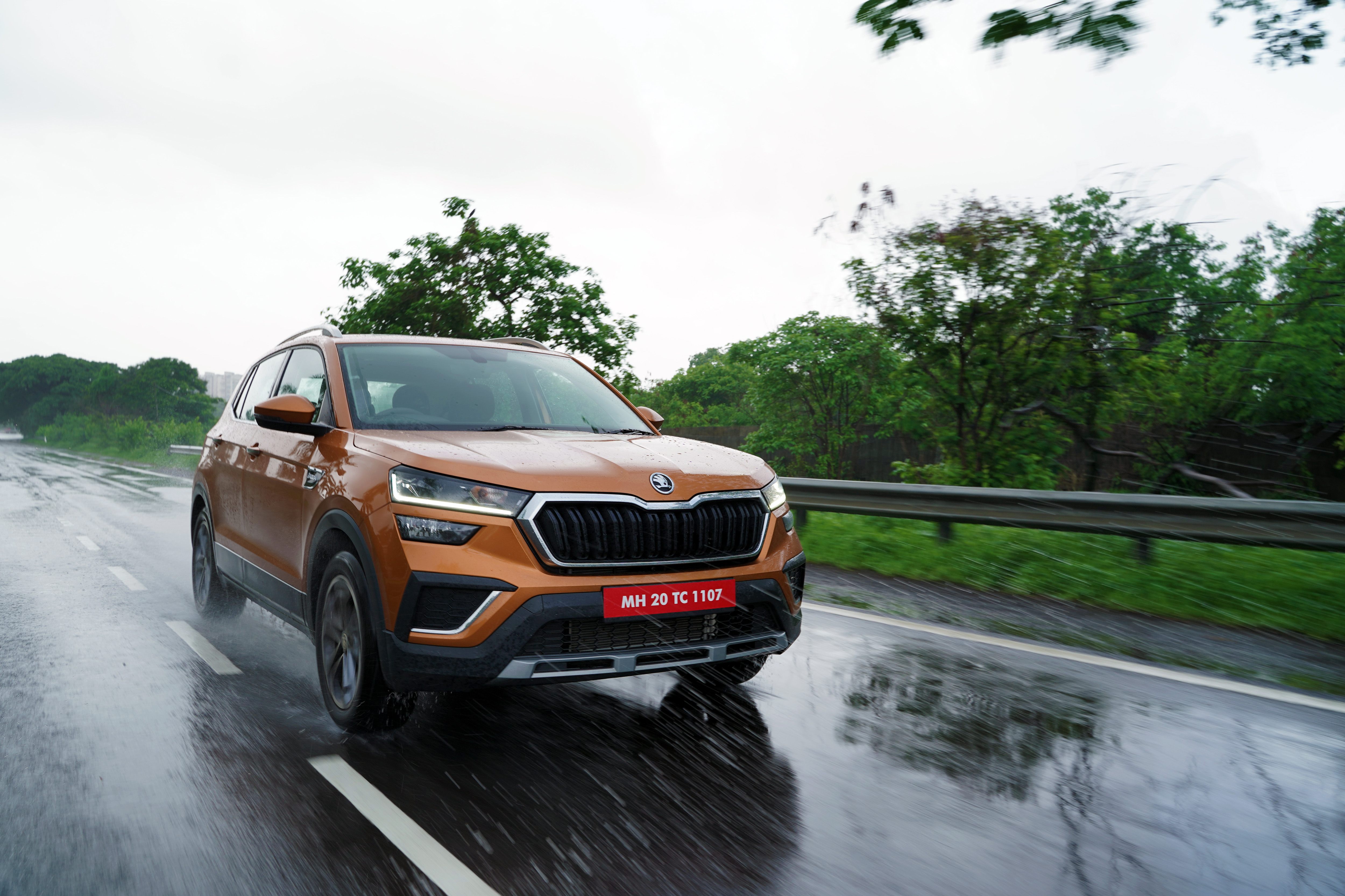 Orange Škoda Kushaq SUV on a rainy road HD Wallpaper