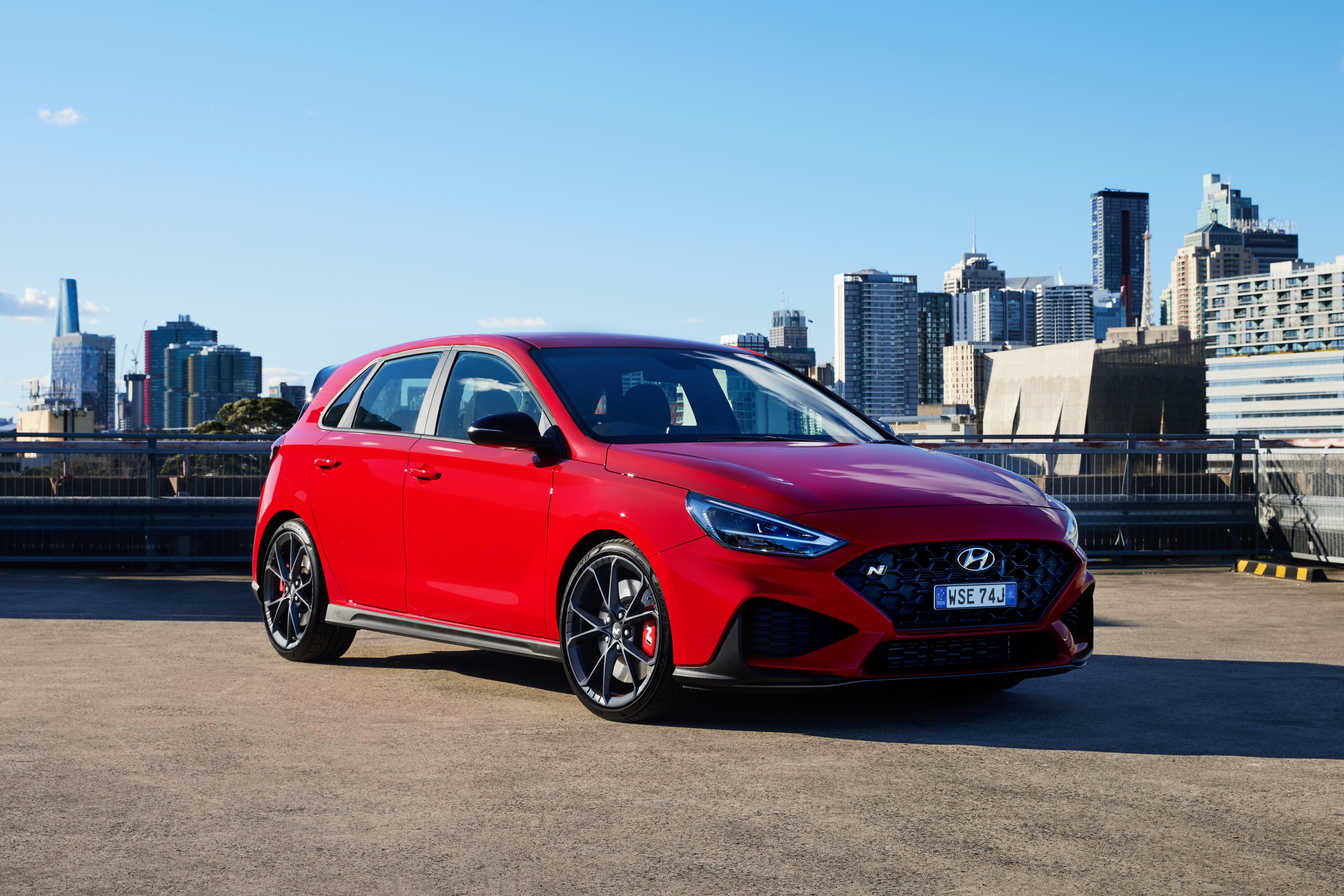 Red Hyundai i30 N on rooftop with city view HD Wallpaper