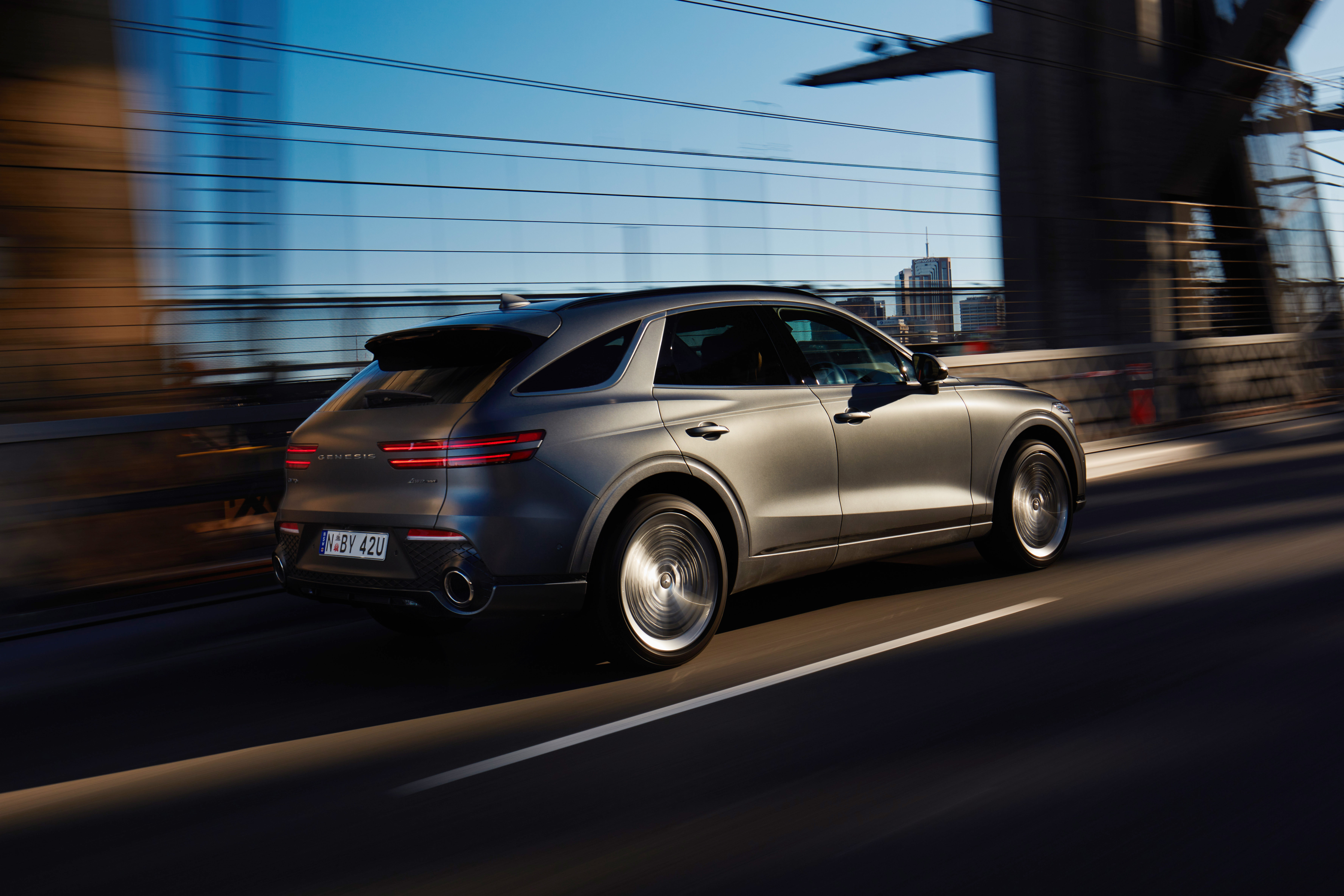Grey Genesis GV70 SUV driving on a city bridge HD Wallpaper