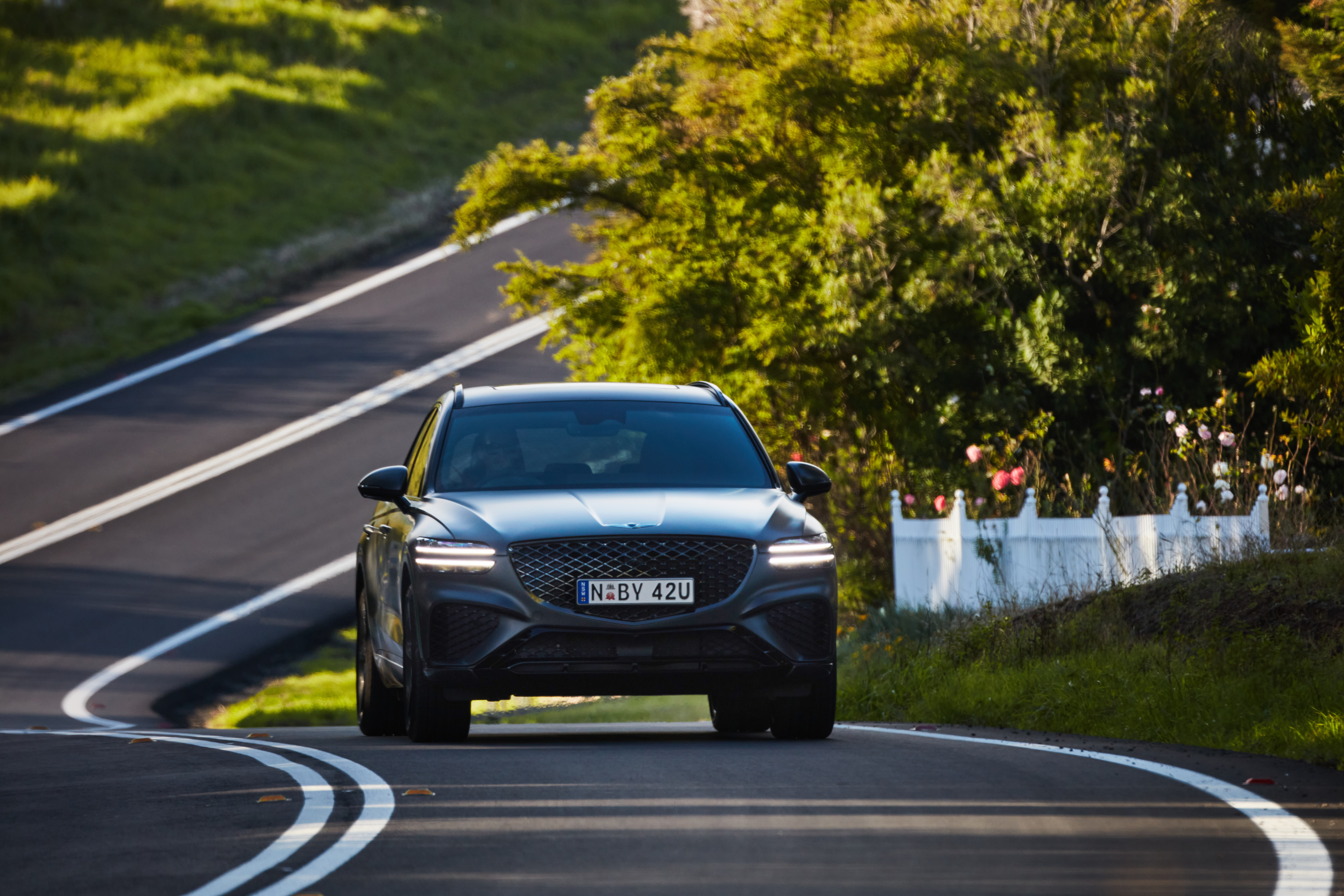 Grey Genesis GV70 SUV driving on a winding road HD Wallpaper
