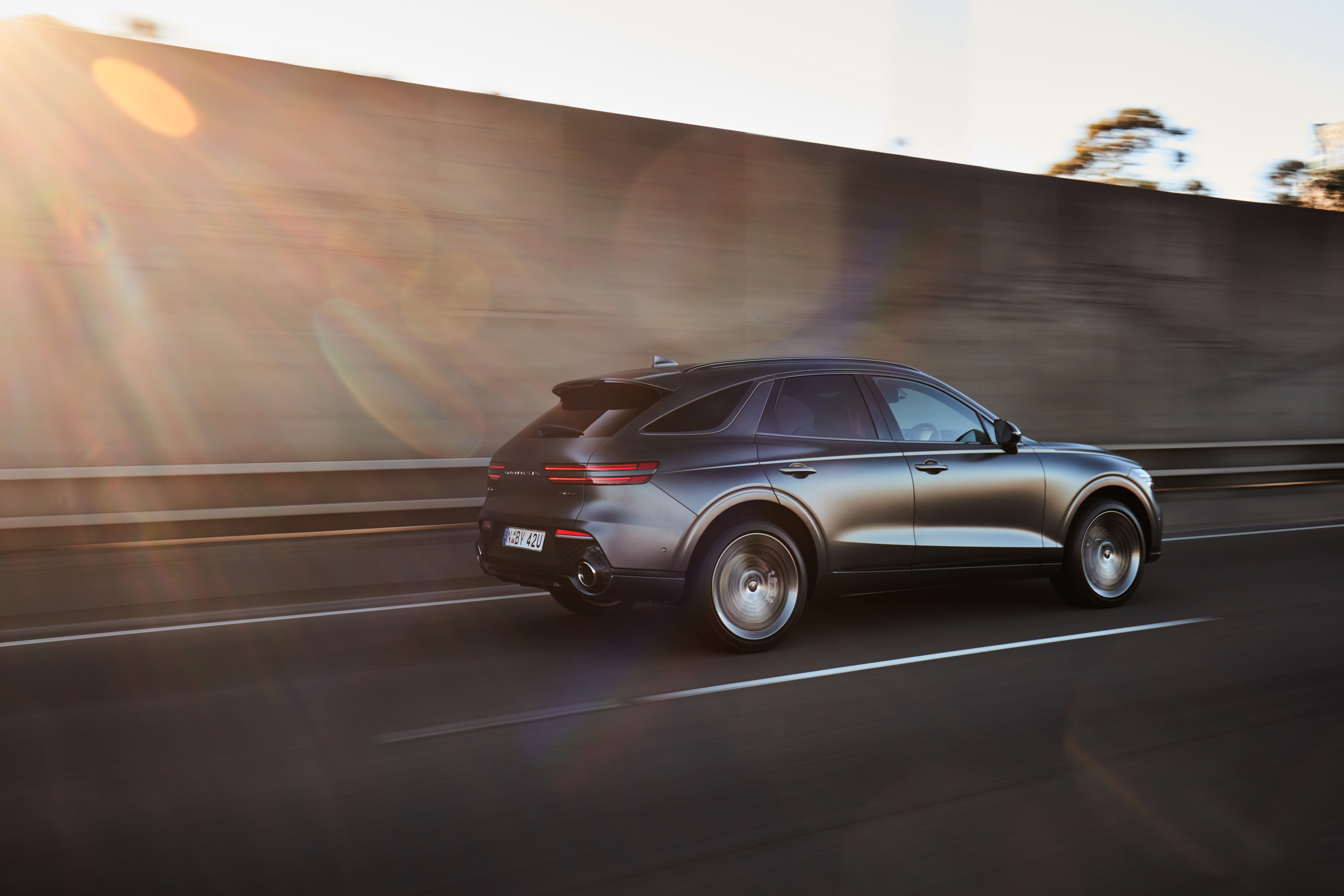 Grey Genesis GV70 SUV driving on a highway at sunset HD Wallpaper