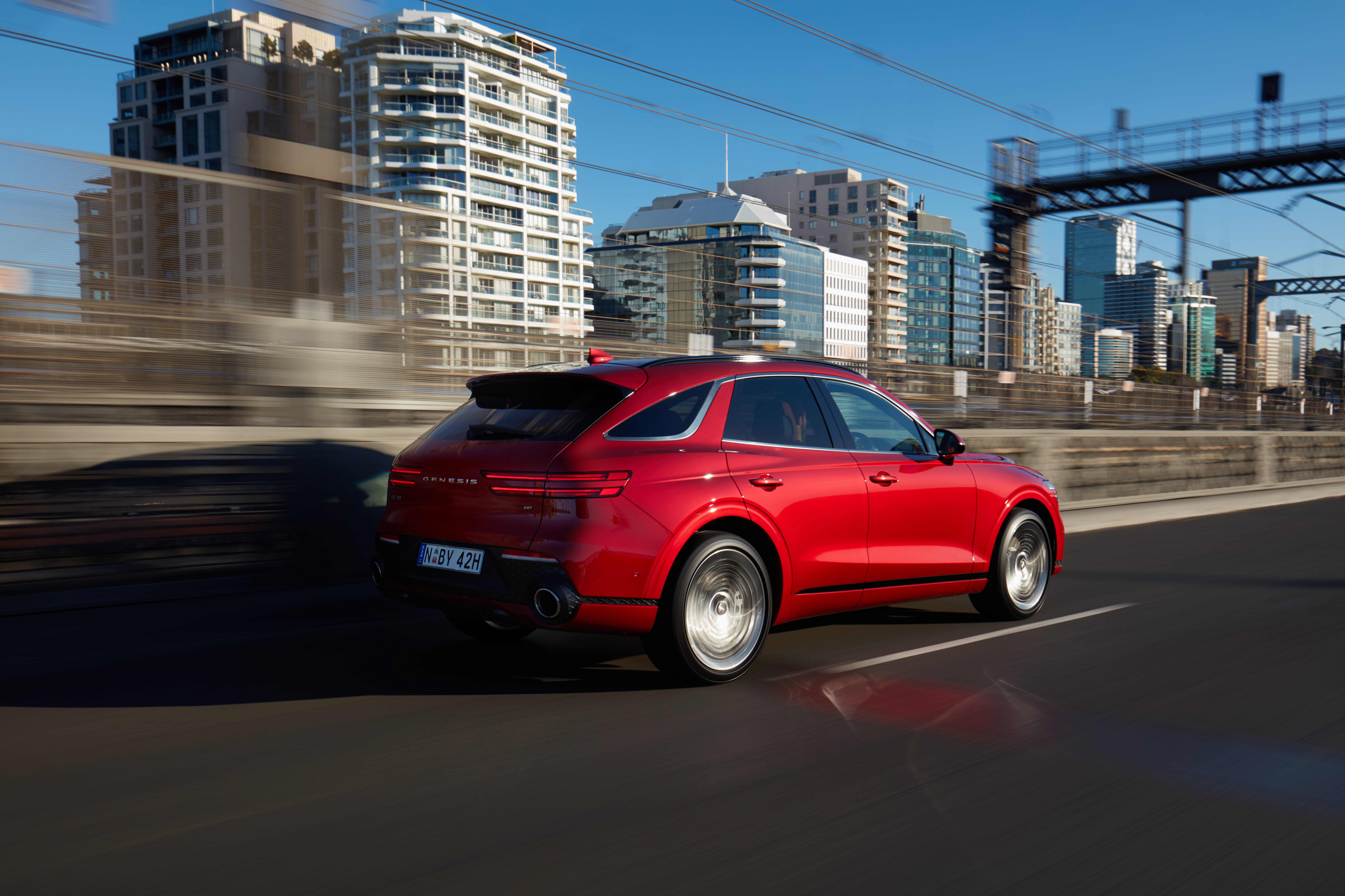 Red Genesis GV70 SUV driving through a city HD Wallpaper