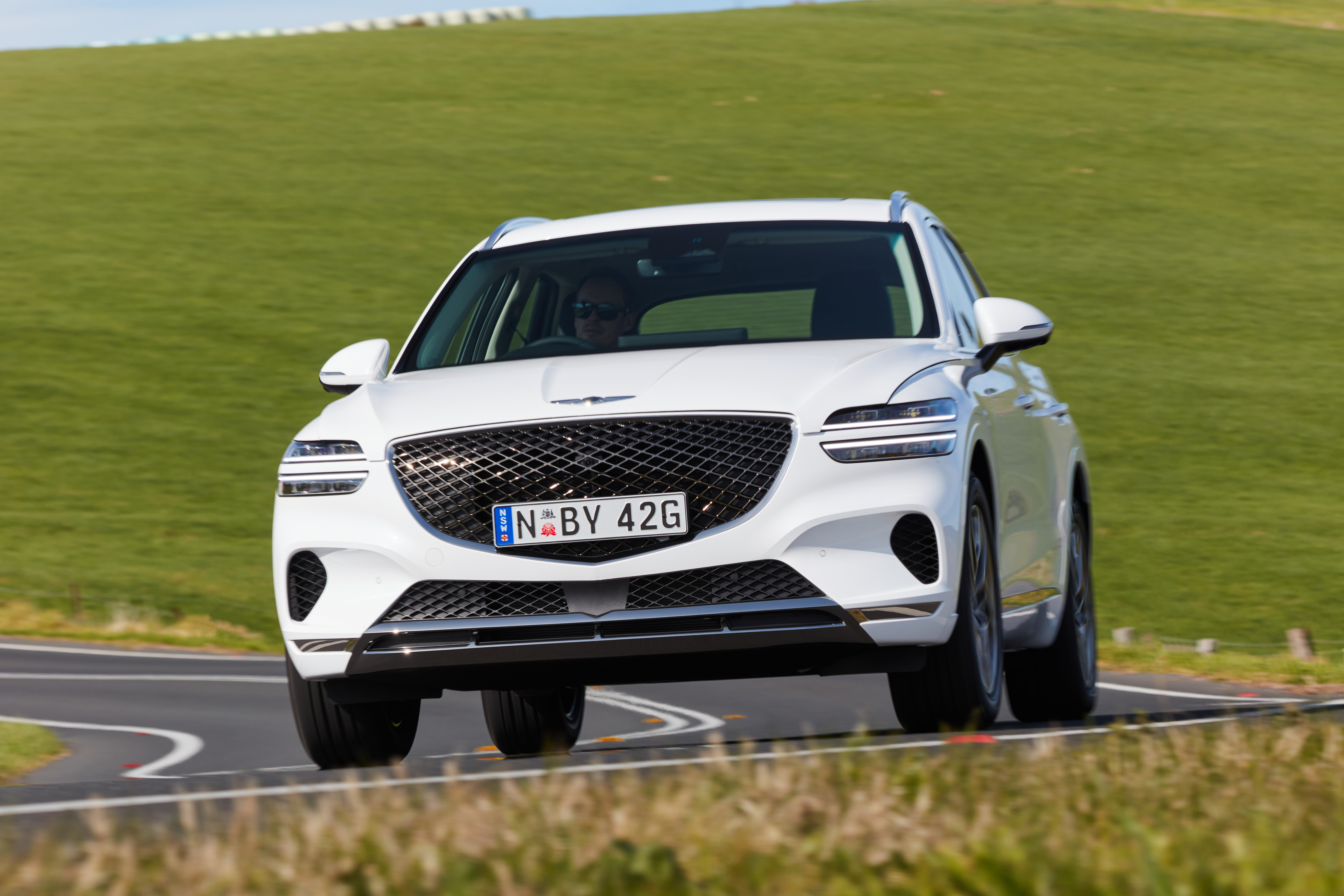 White Genesis GV70 SUV driving on a winding road HD Wallpaper