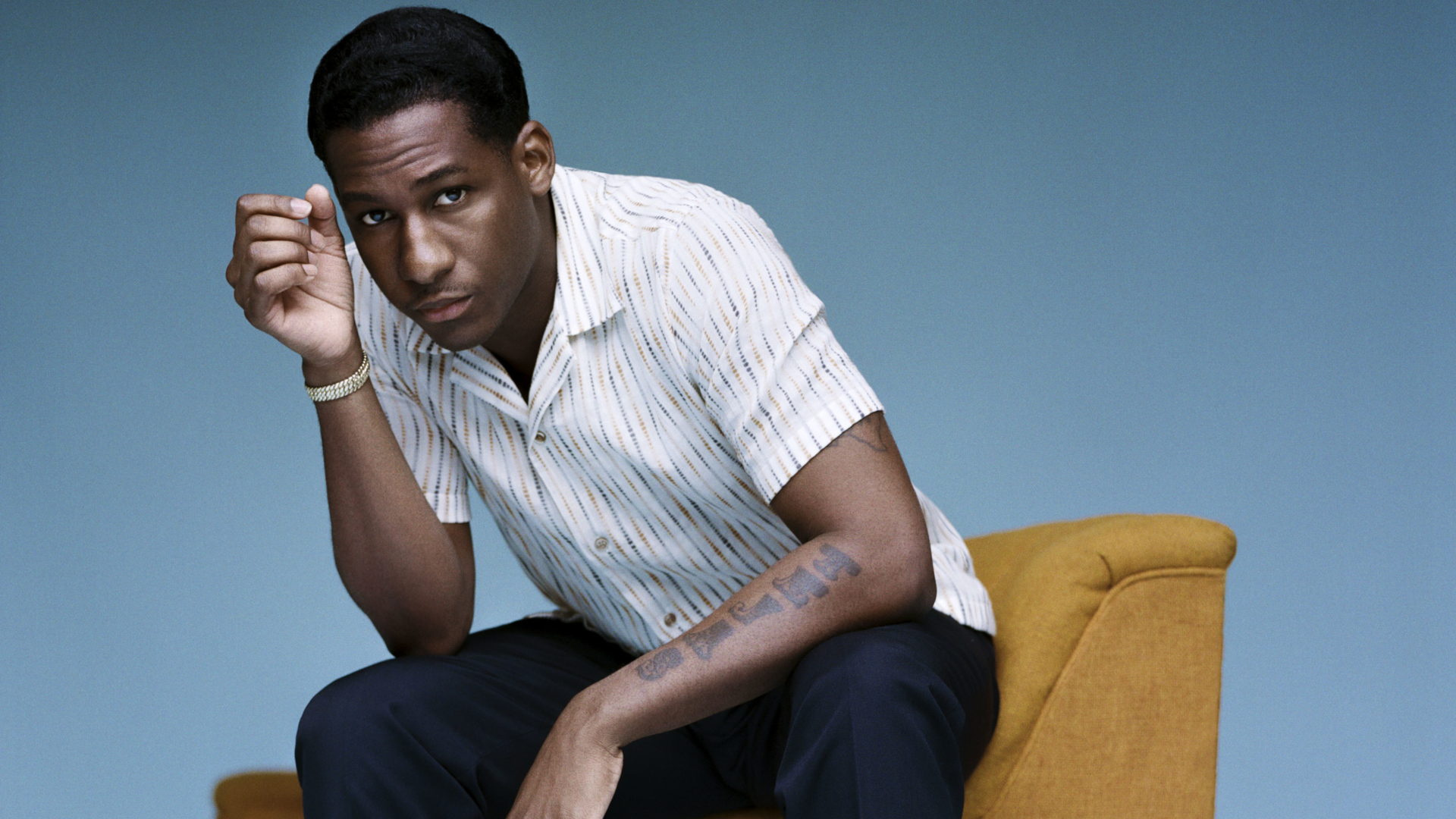 Leon Bridges sitting on yellow chair against blue background HD Wallpaper