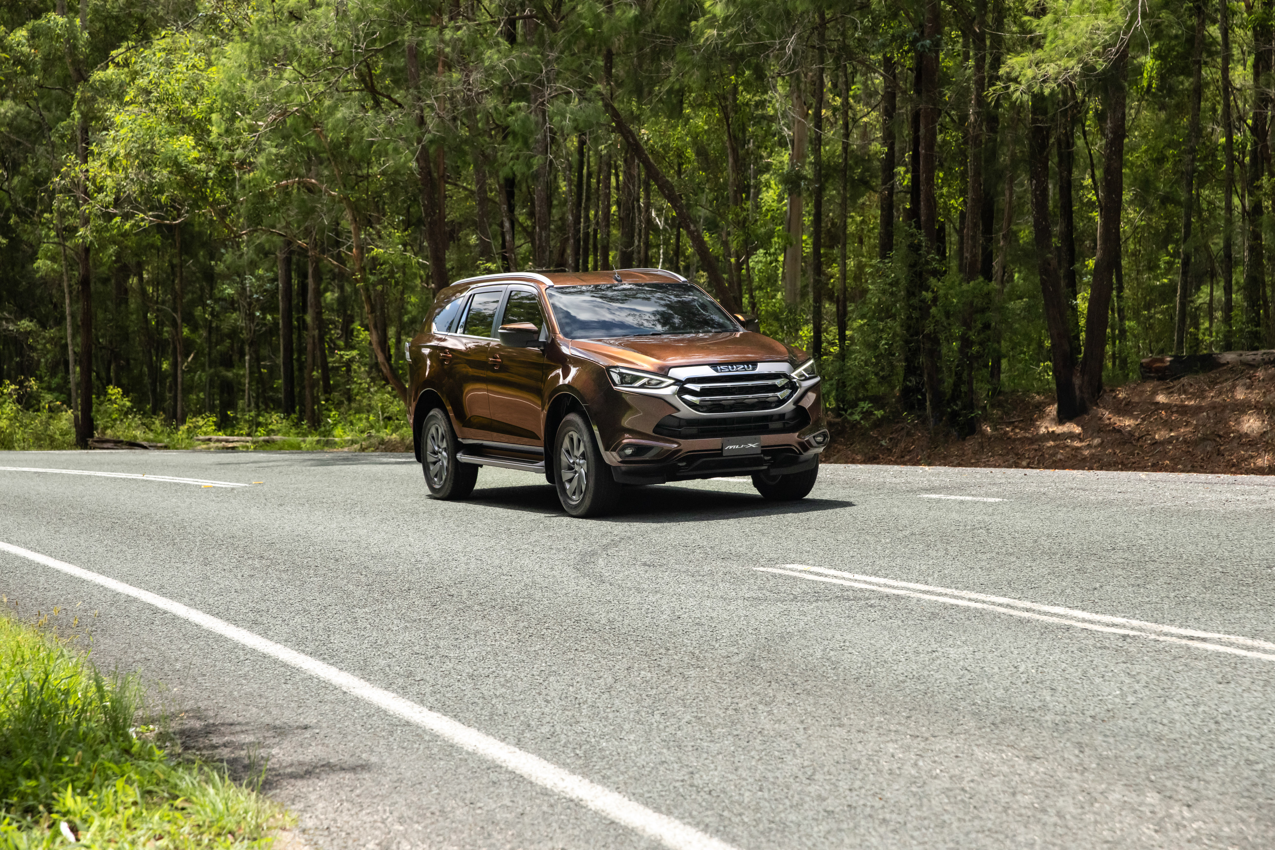 Brown Isuzu MU-X SUV on a road surrounded by trees HD Wallpaper