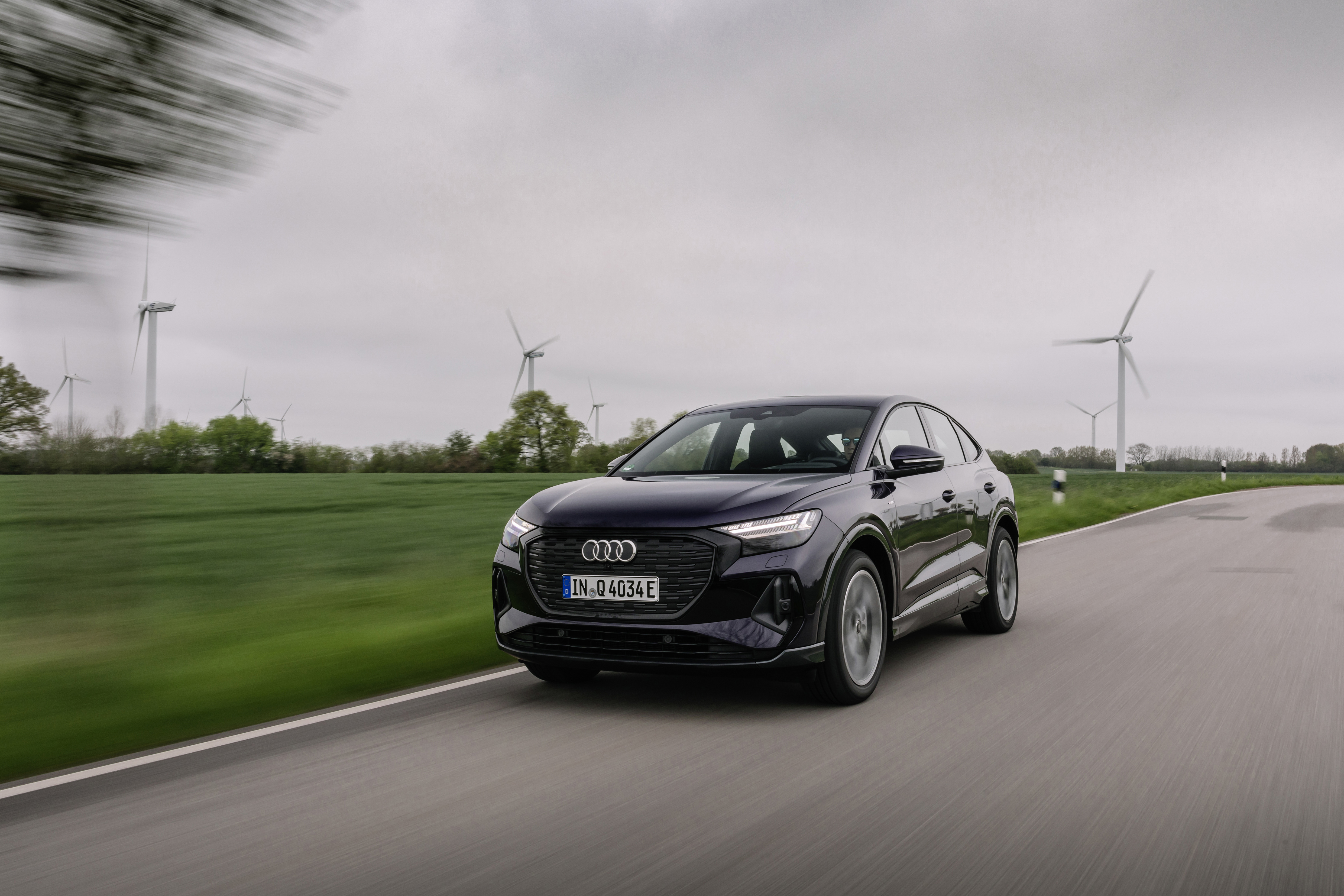 Audi Q4 Sportback e-tron Electric SUV driving past wind turbines HD Wallpaper
