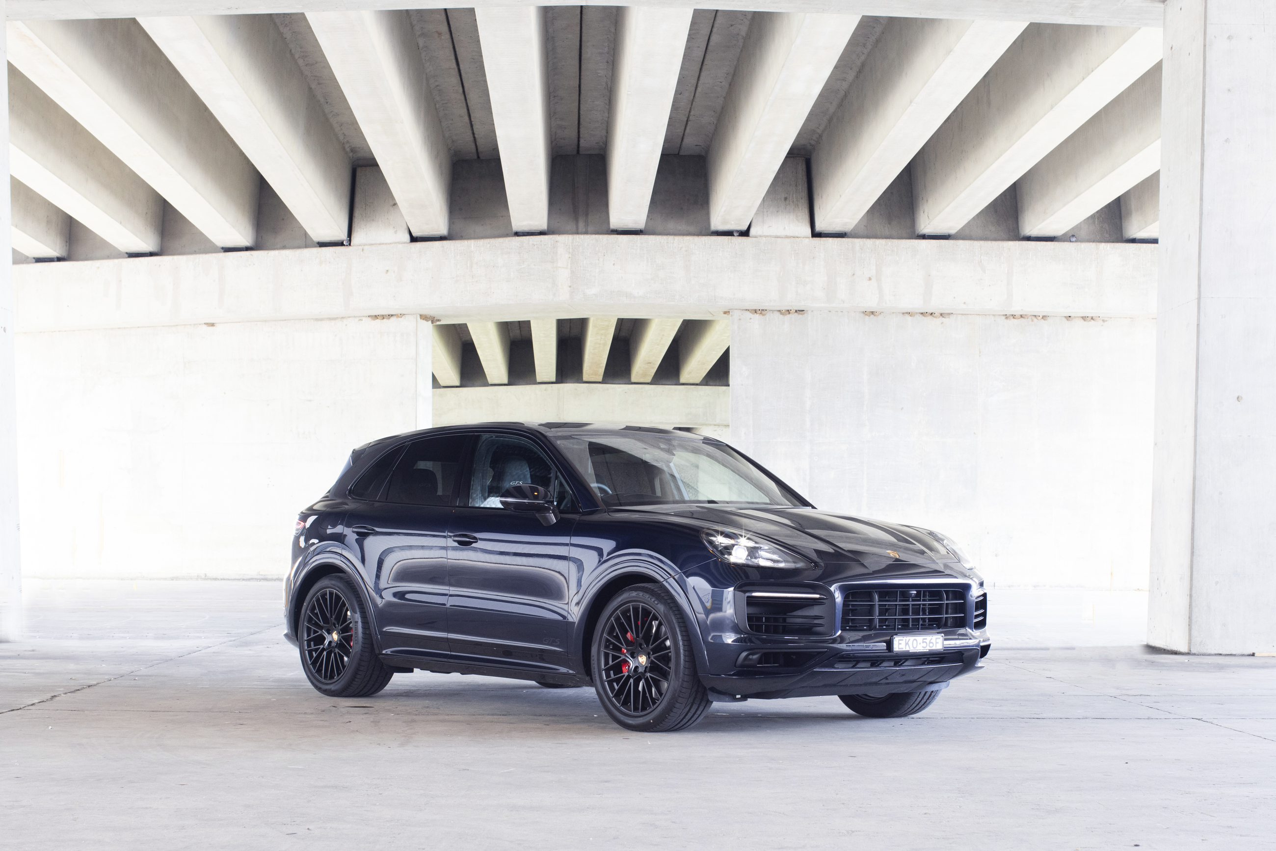 Dark Porsche Cayenne GTS SUV parked under concrete structure HD Wallpaper