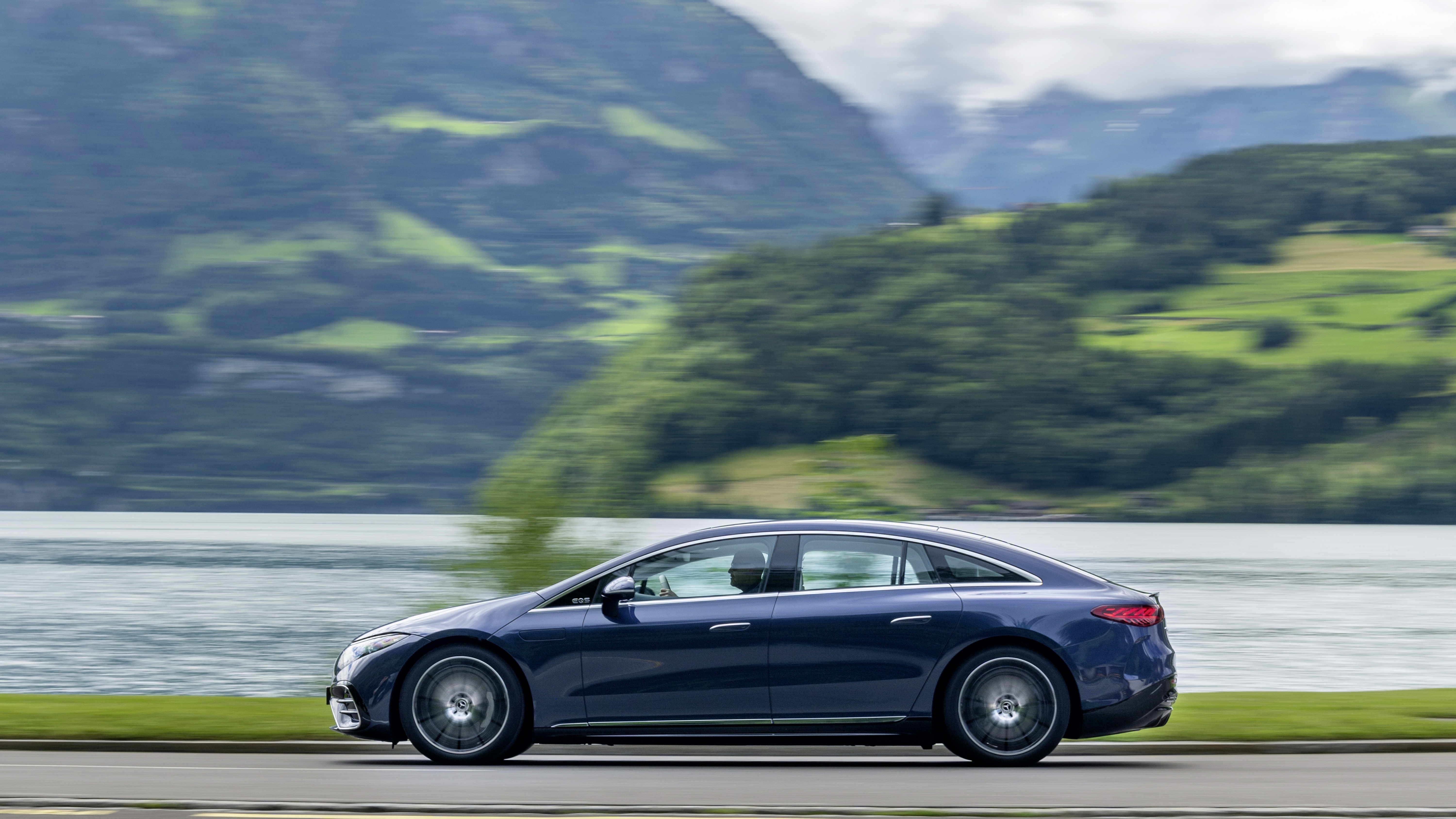 Blue Mercedes-Benz EQS driving by a lake HD Wallpaper