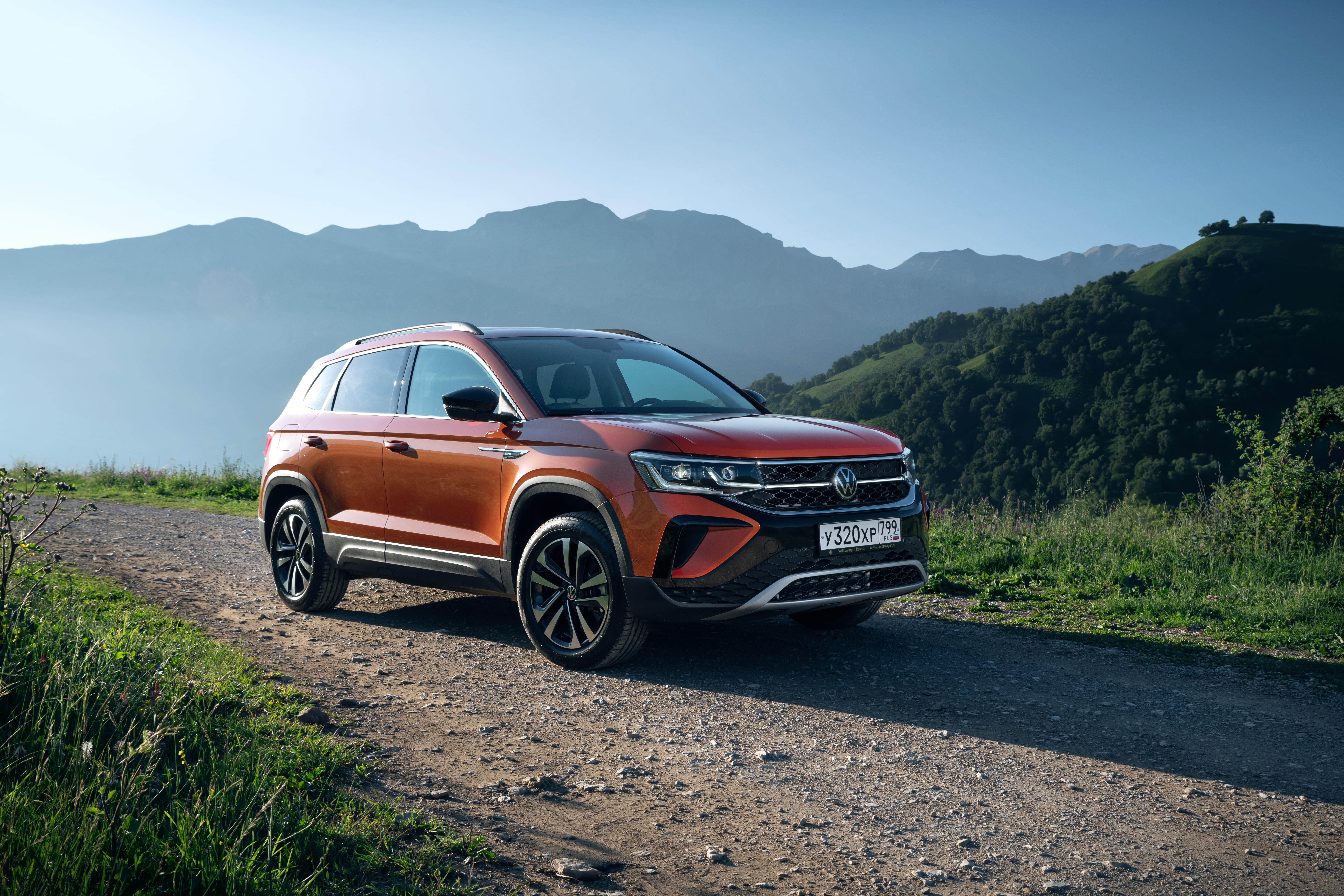 Orange Volkswagen Taos SUV on a scenic mountain road HD Wallpaper