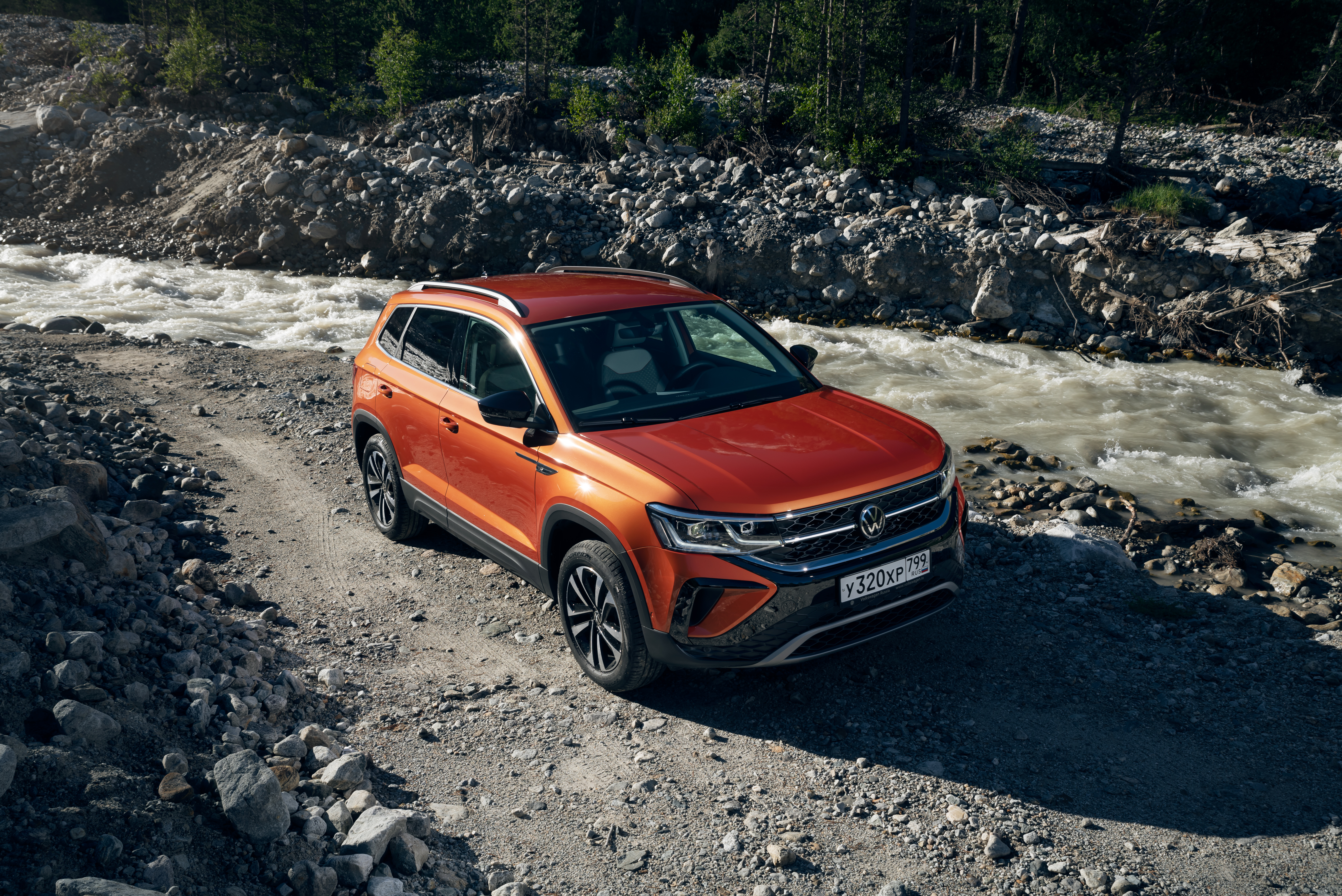 Orange Volkswagen Taos SUV off-roading by a river HD Wallpaper