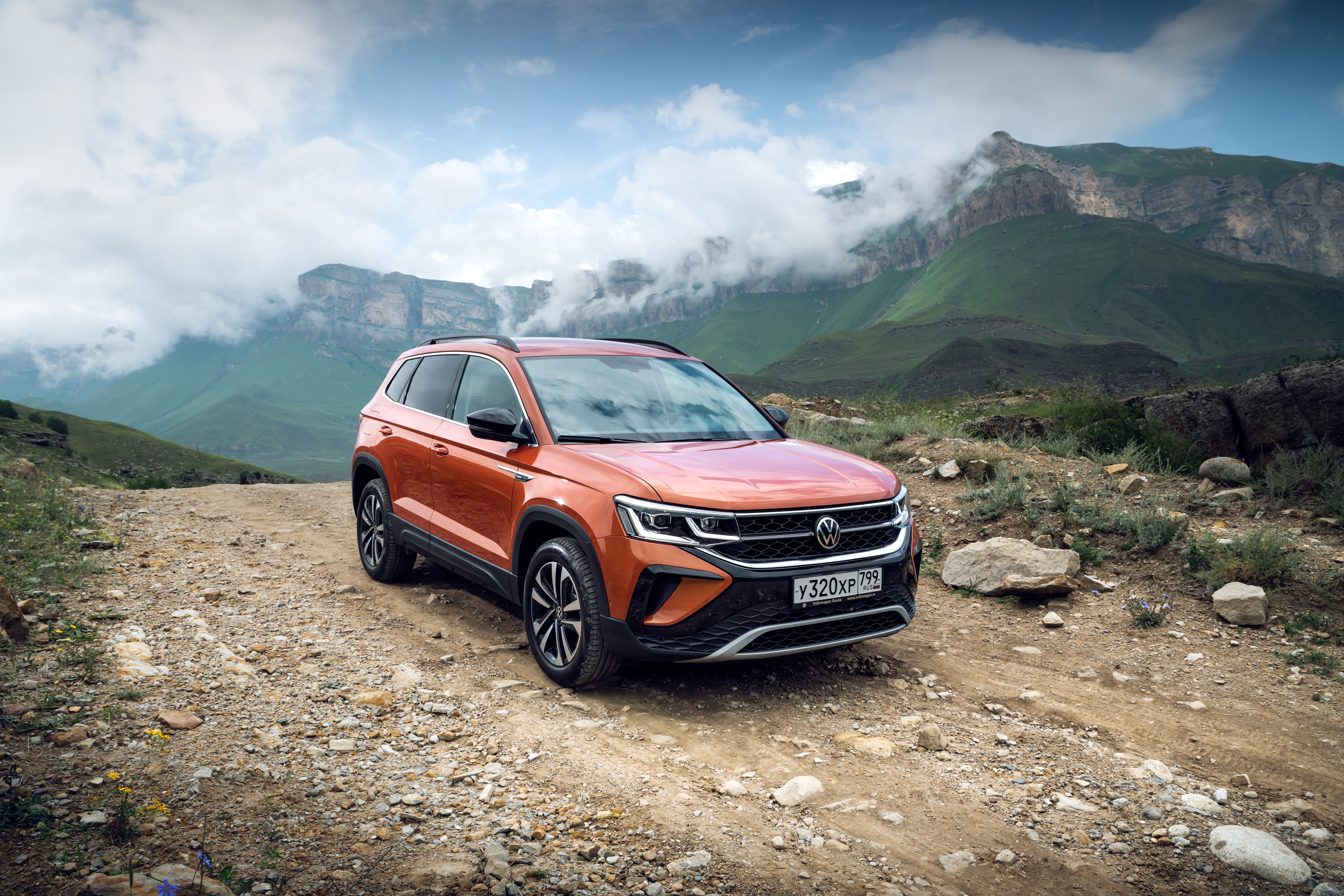 Orange Volkswagen Taos SUV in cloudy mountain landscape HD Wallpaper