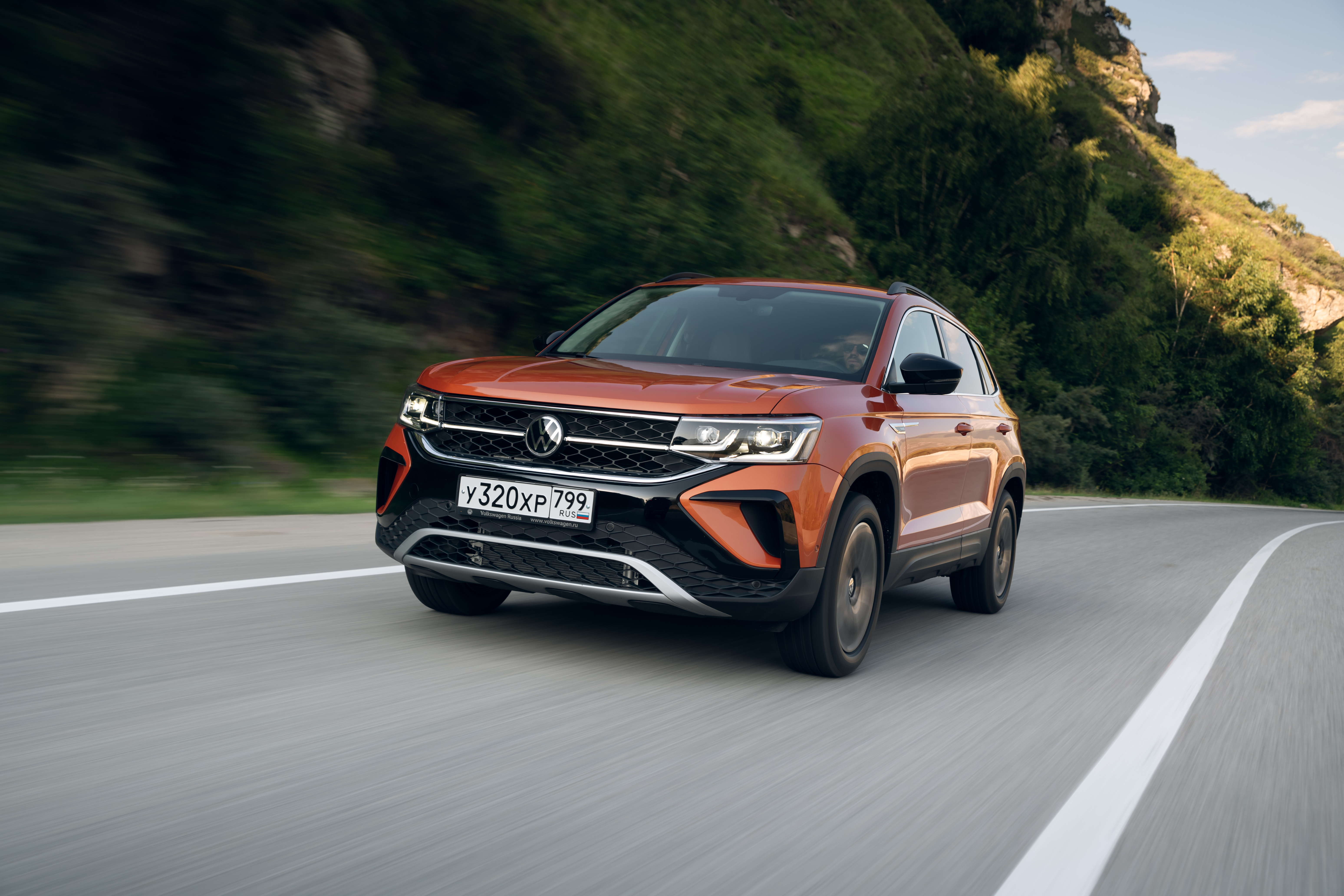 Orange Volkswagen Taos SUV driving on a scenic road HD Wallpaper