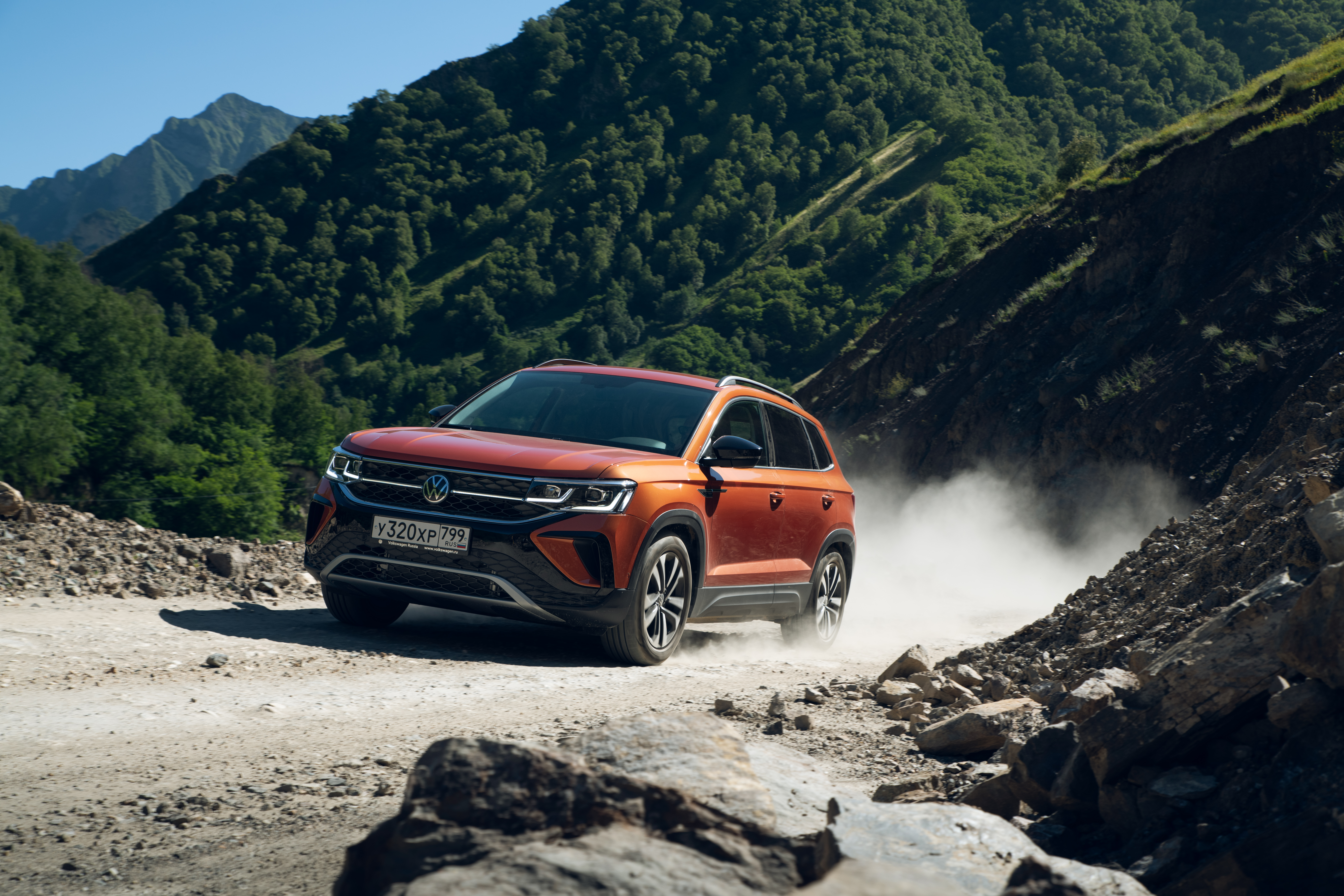 Orange Volkswagen Taos SUV driving on dusty mountain road HD Wallpaper
