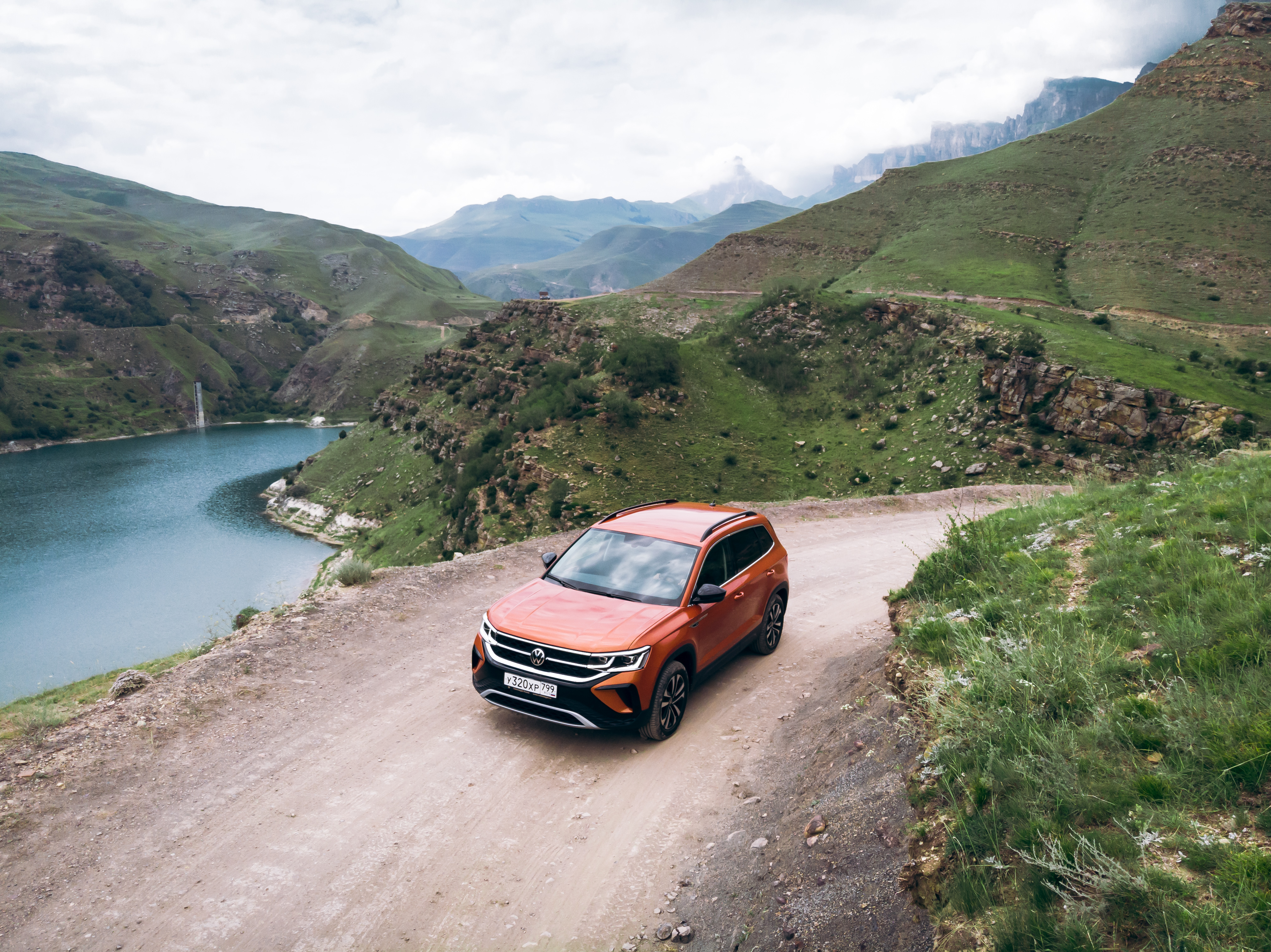 Orange Volkswagen Taos SUV on a scenic mountain road HD Wallpaper