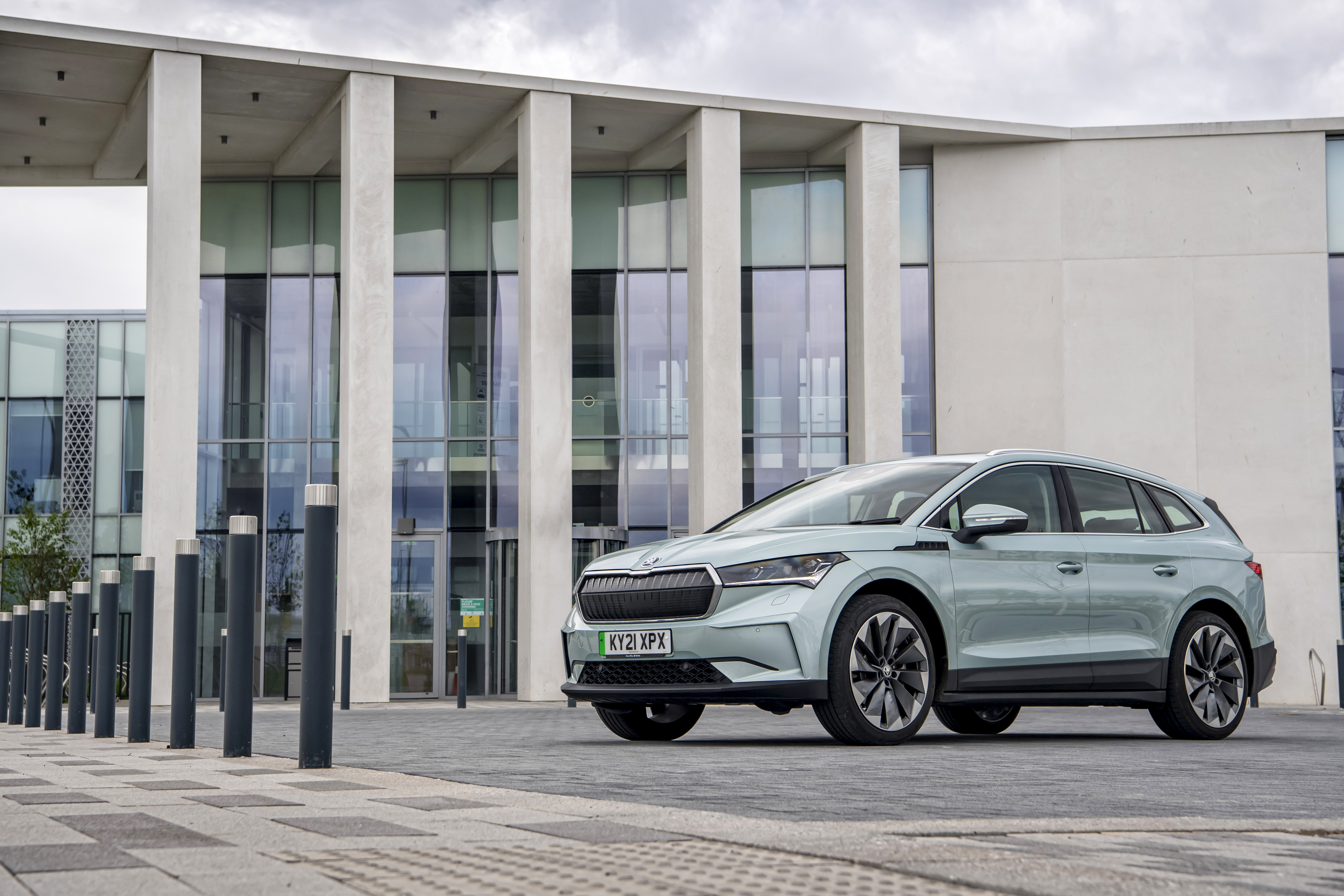 Škoda Enyaq Electric SUV in front of a modern building HD Wallpaper