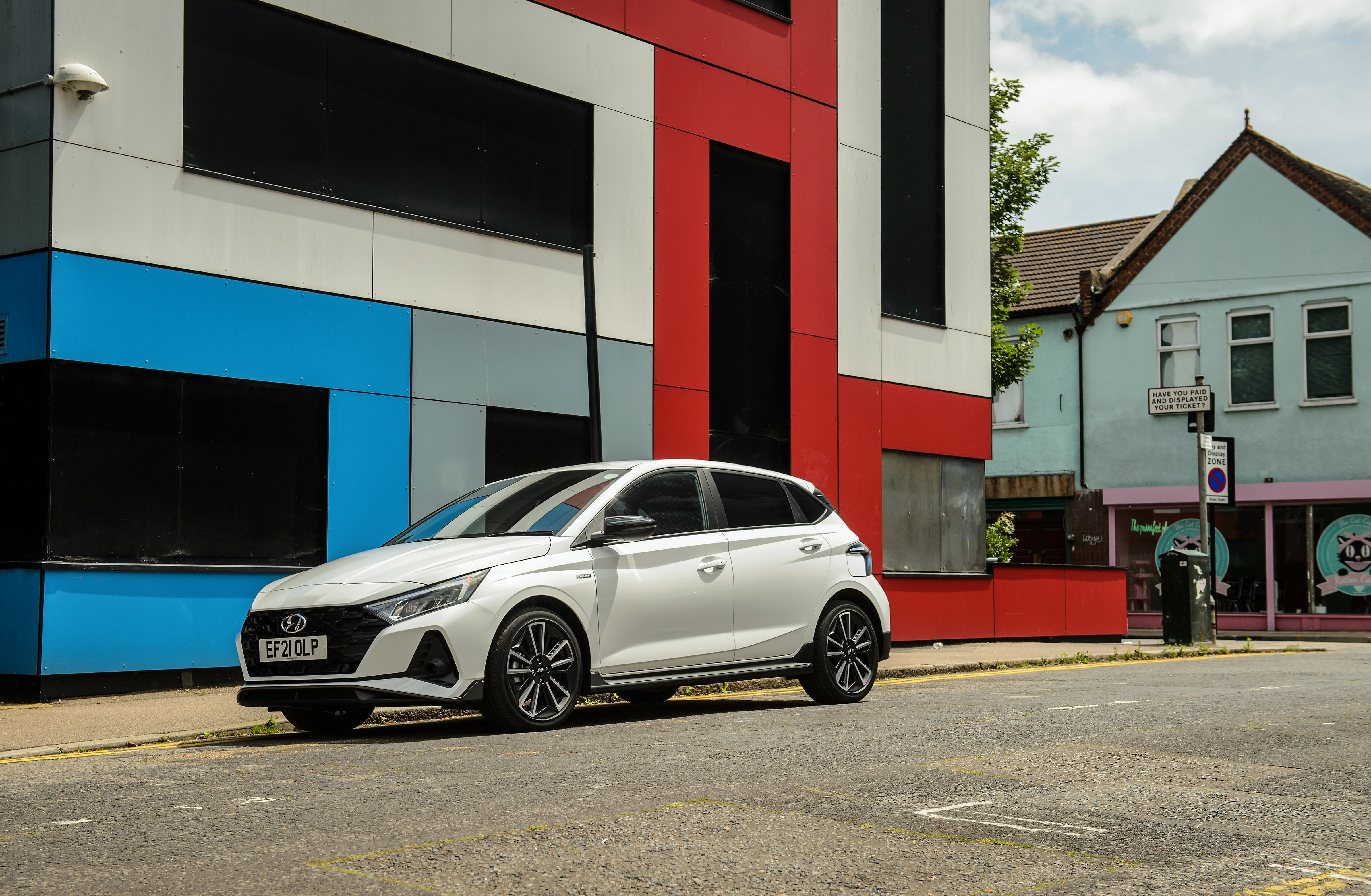 White Hyundai i20 N Line on a street with colorful buildings HD Wallpaper