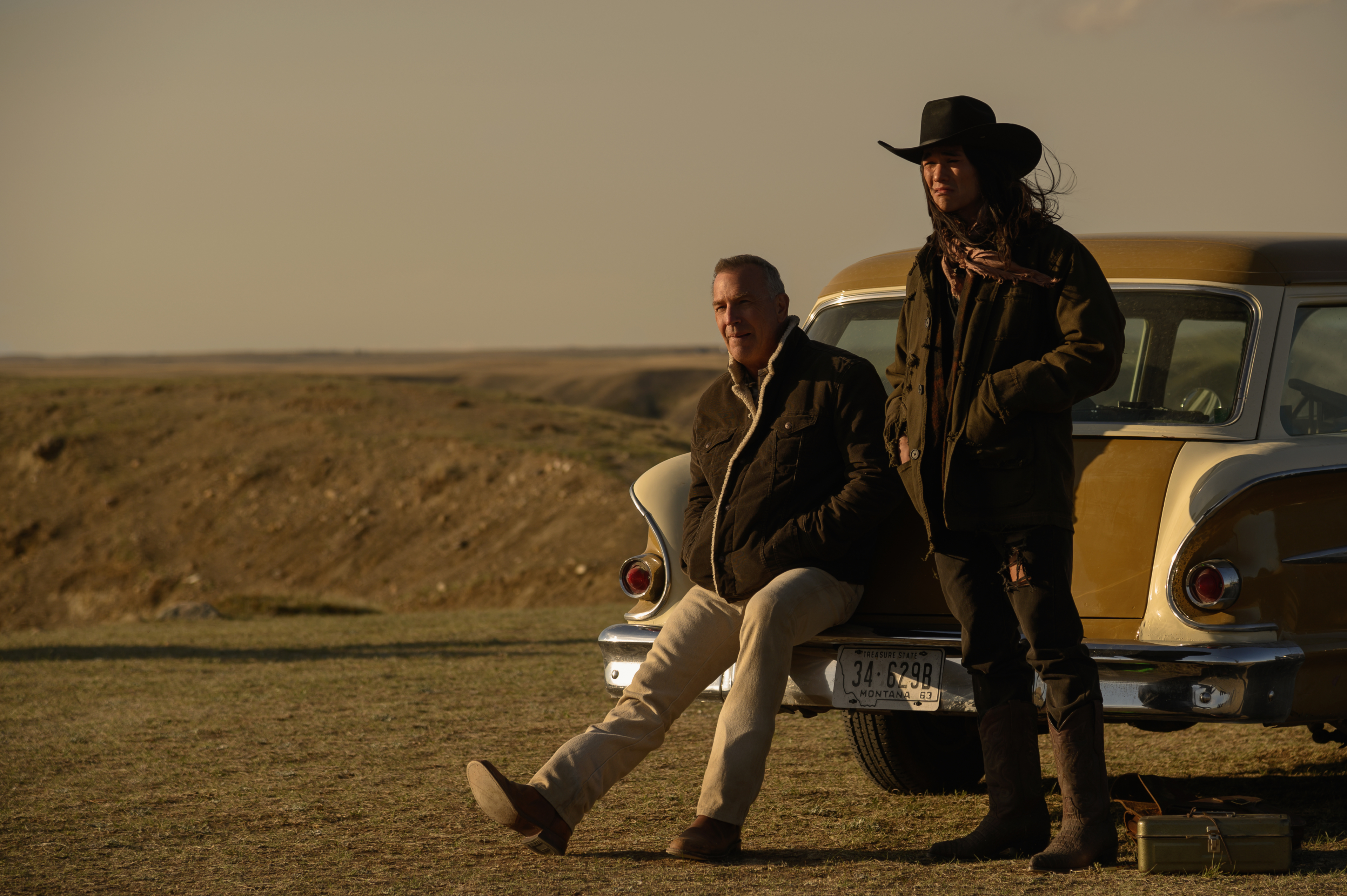 Kevin Costner and Booboo Stewart by vintage car in western landscape HD Wallpaper