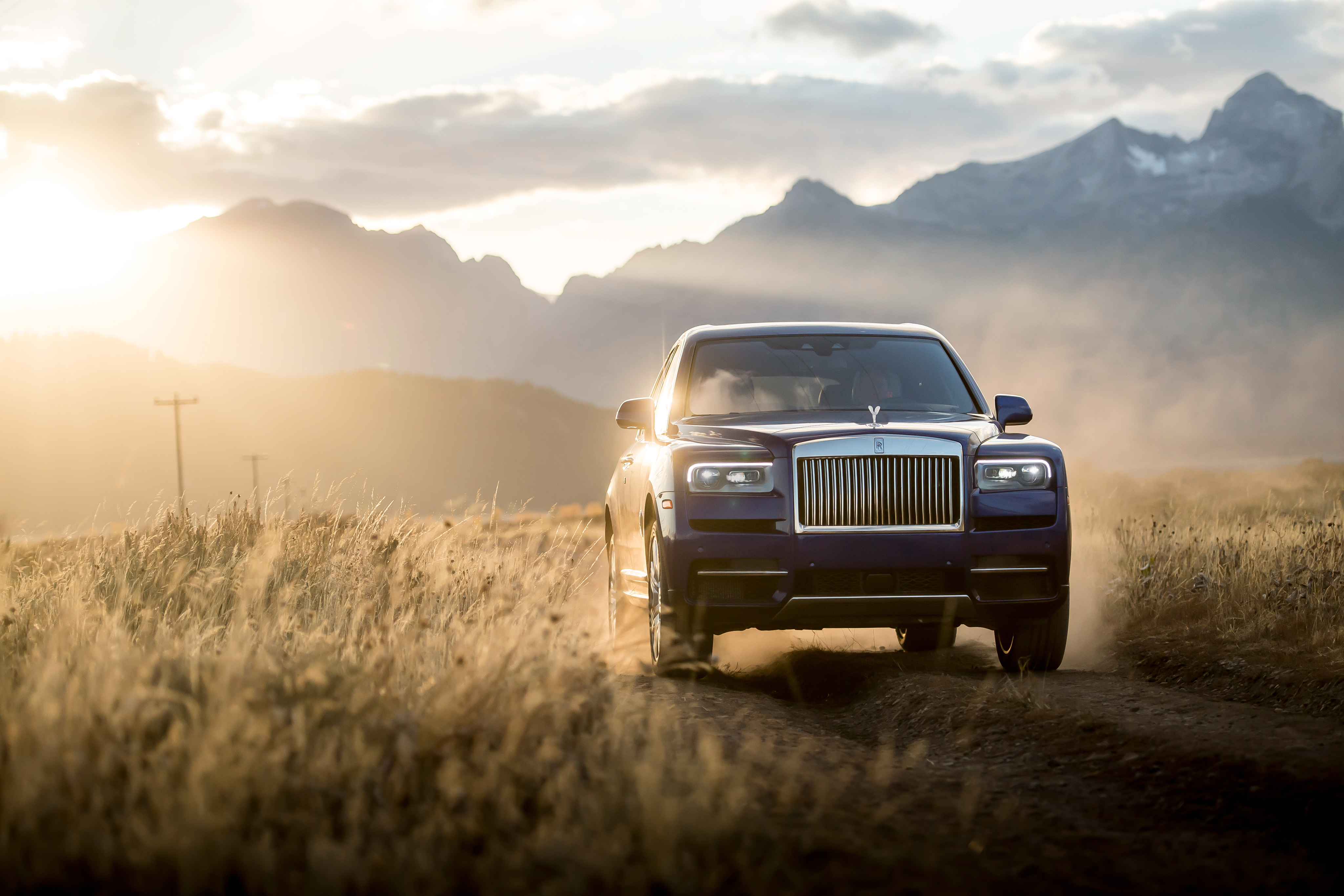 Rolls-Royce Cullinan SUV driving through mountains at golden hour HD Wallpaper