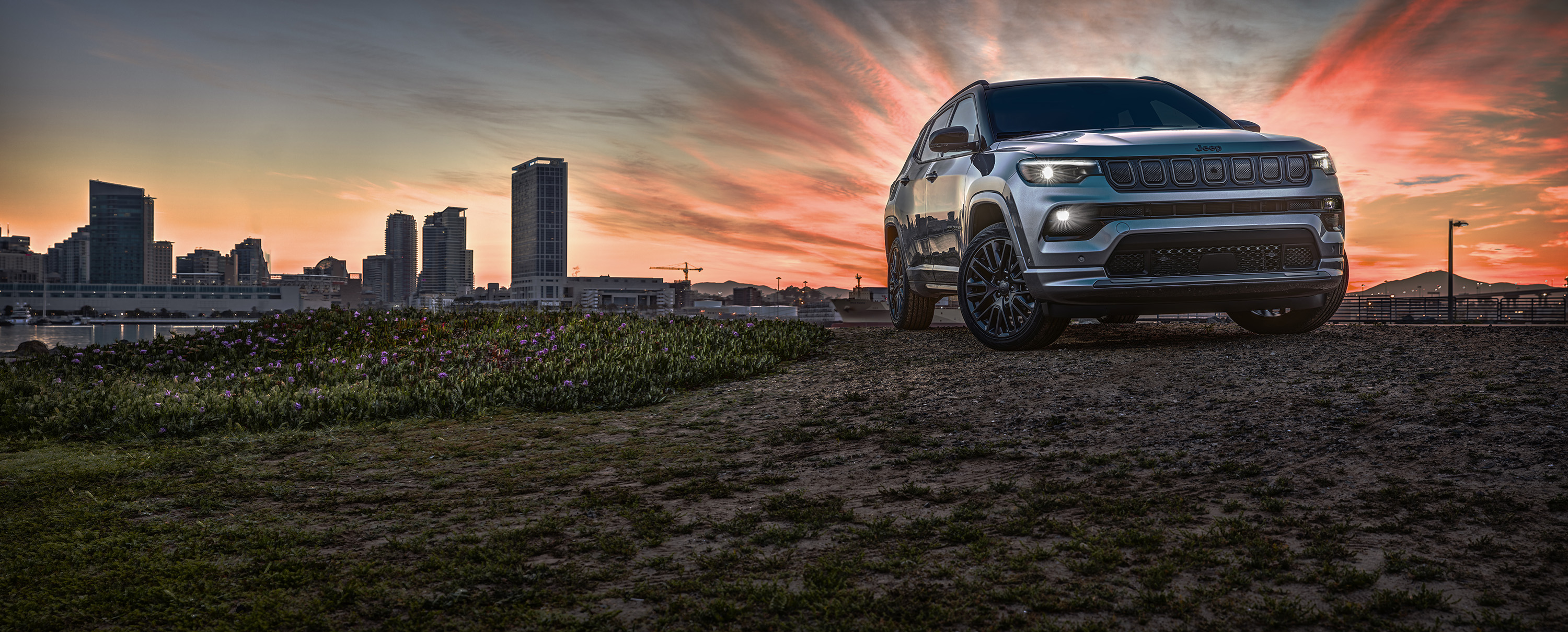 Silver Jeep Compass High Altitude SUV at sunset with city skyline HD Wallpaper