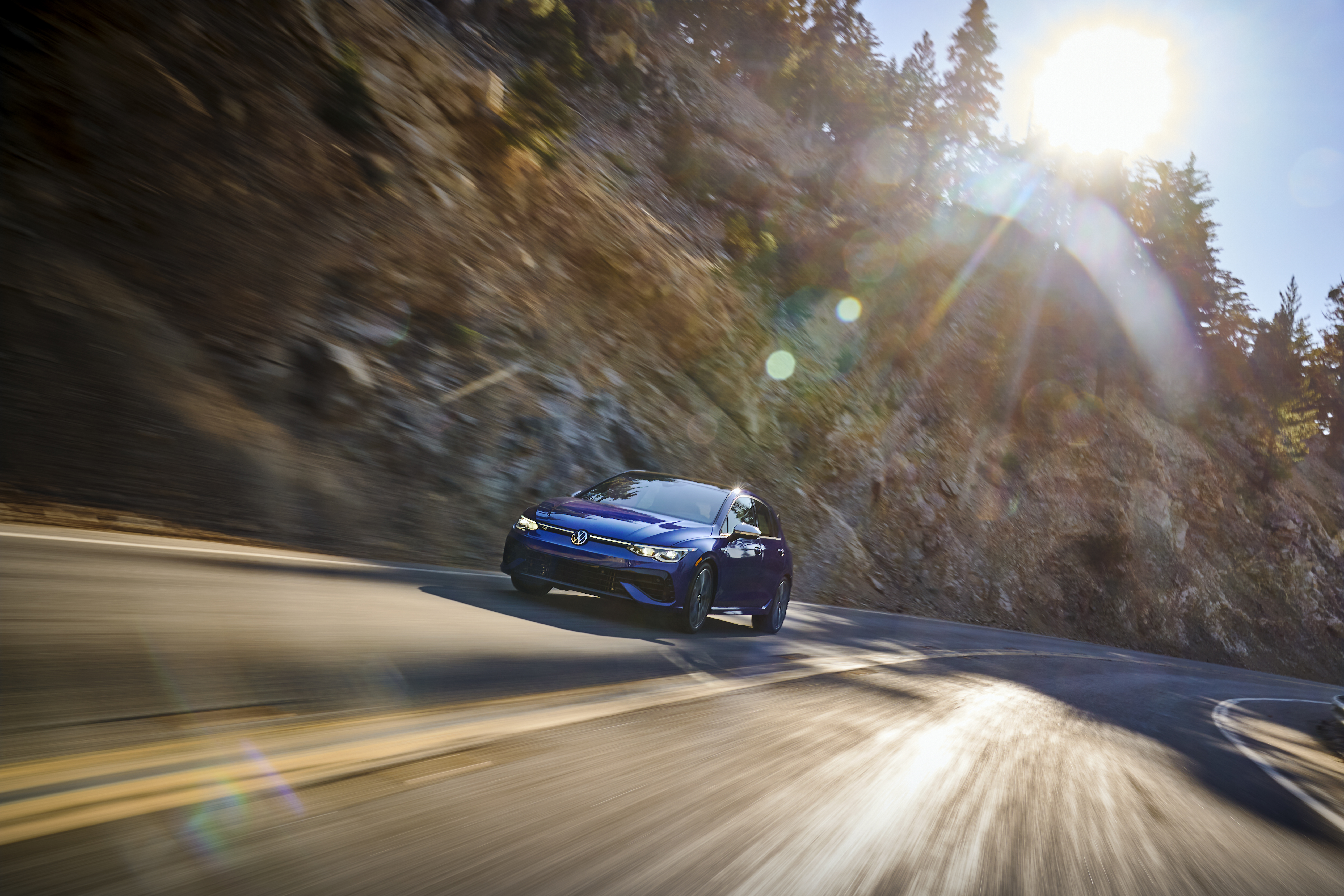 Blue Volkswagen Golf R speeding on a sunny mountain road HD Wallpaper