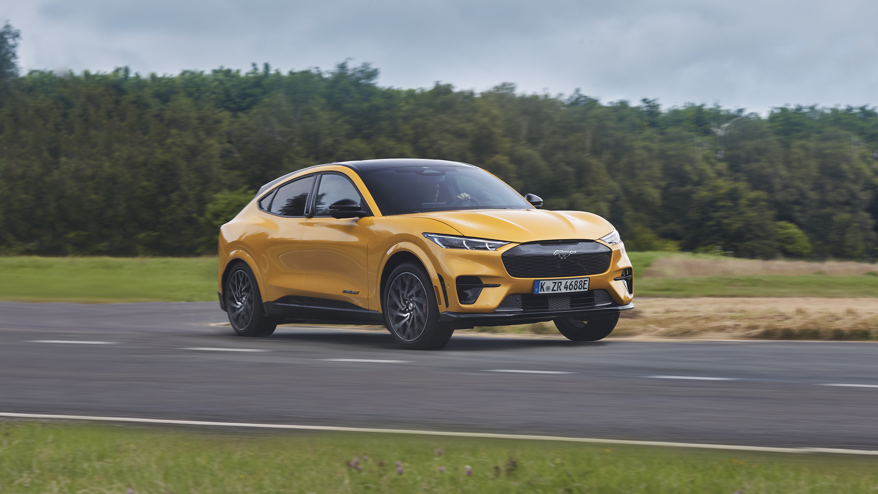 Orange Ford Mustang Mach-E GT driving on a road HD Wallpaper