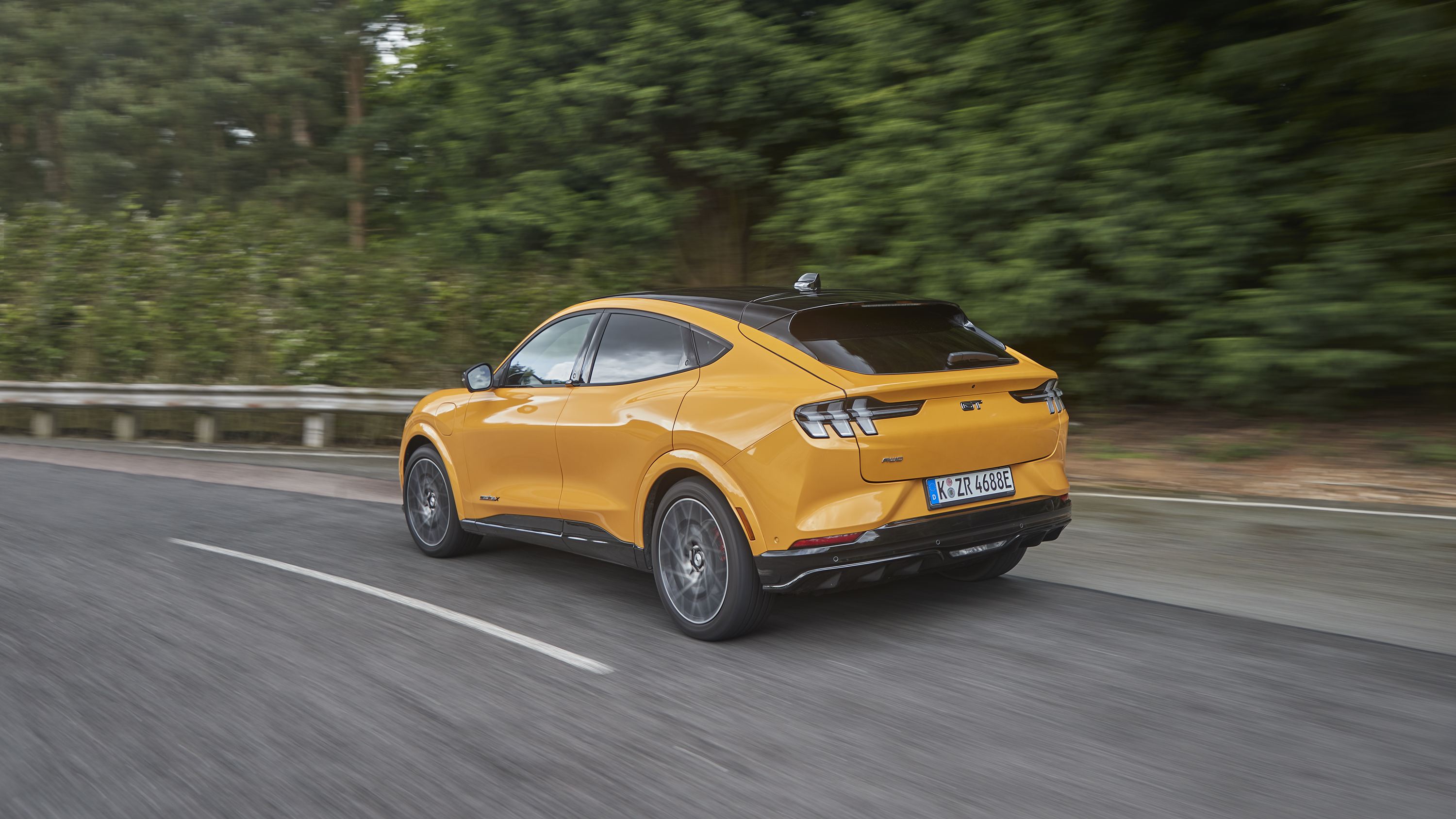 Orange Ford Mustang Mach-E GT driving on a road HD Wallpaper