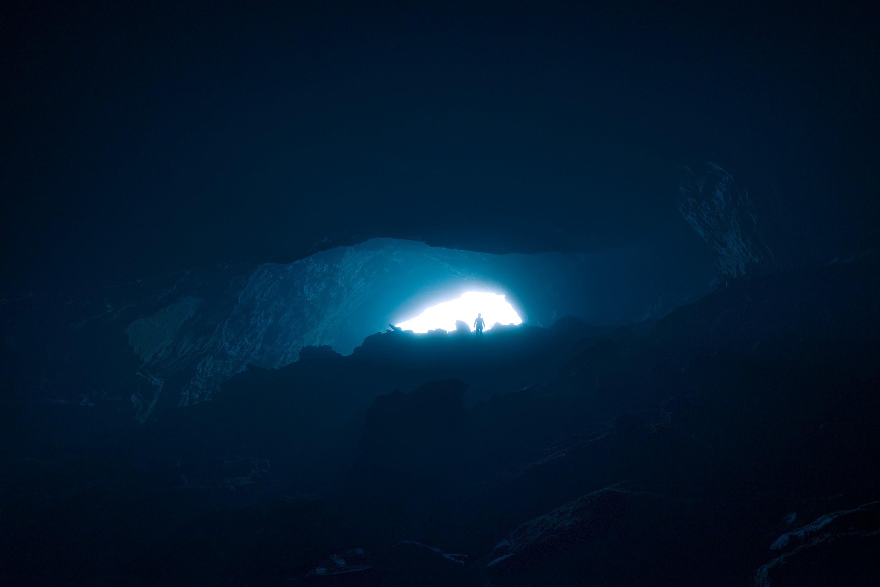 Silhouette of a person in a dark cave entrance HD Wallpaper
