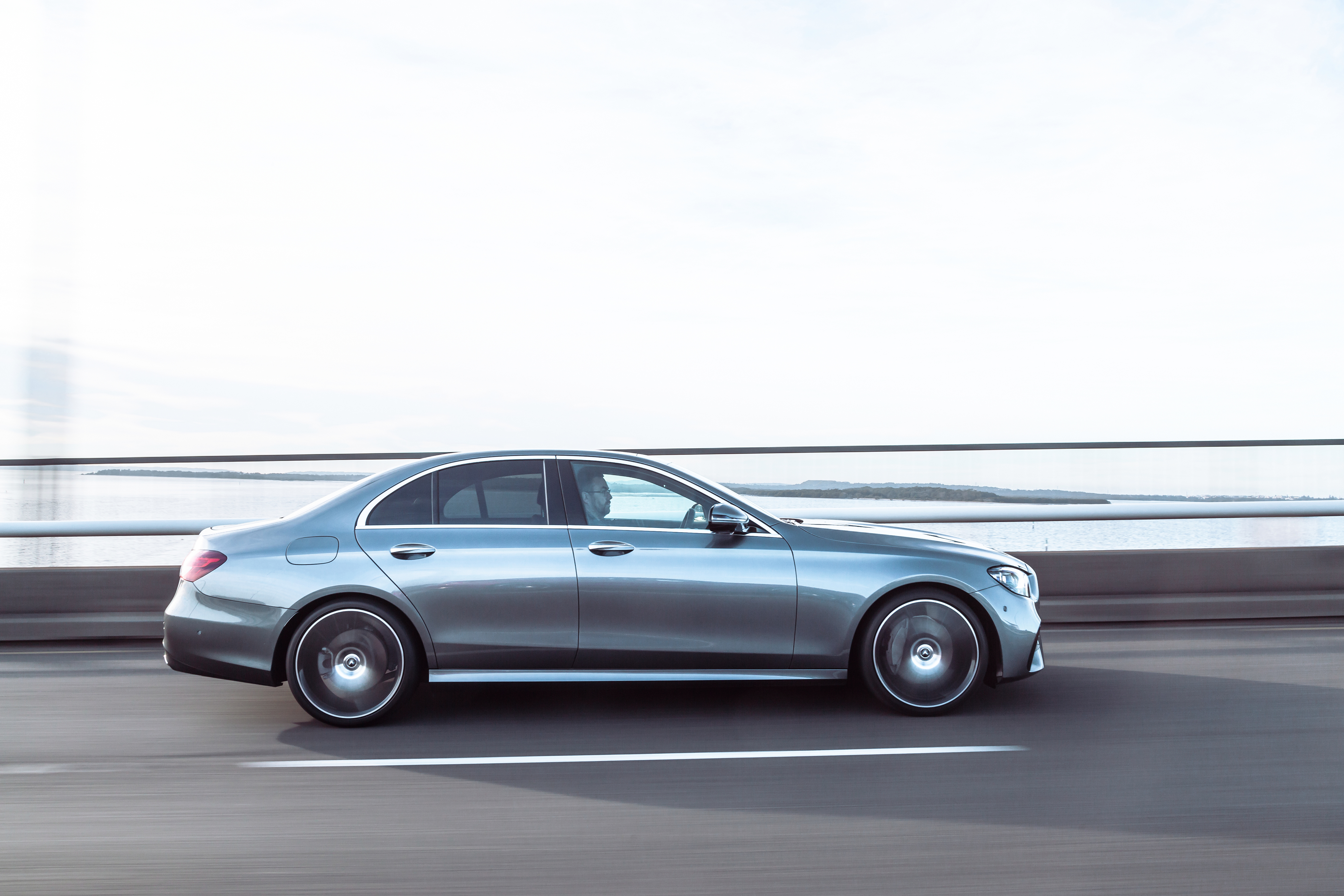 Silver Mercedes-Benz E 350 AMG Line driving on a bridge HD Wallpaper