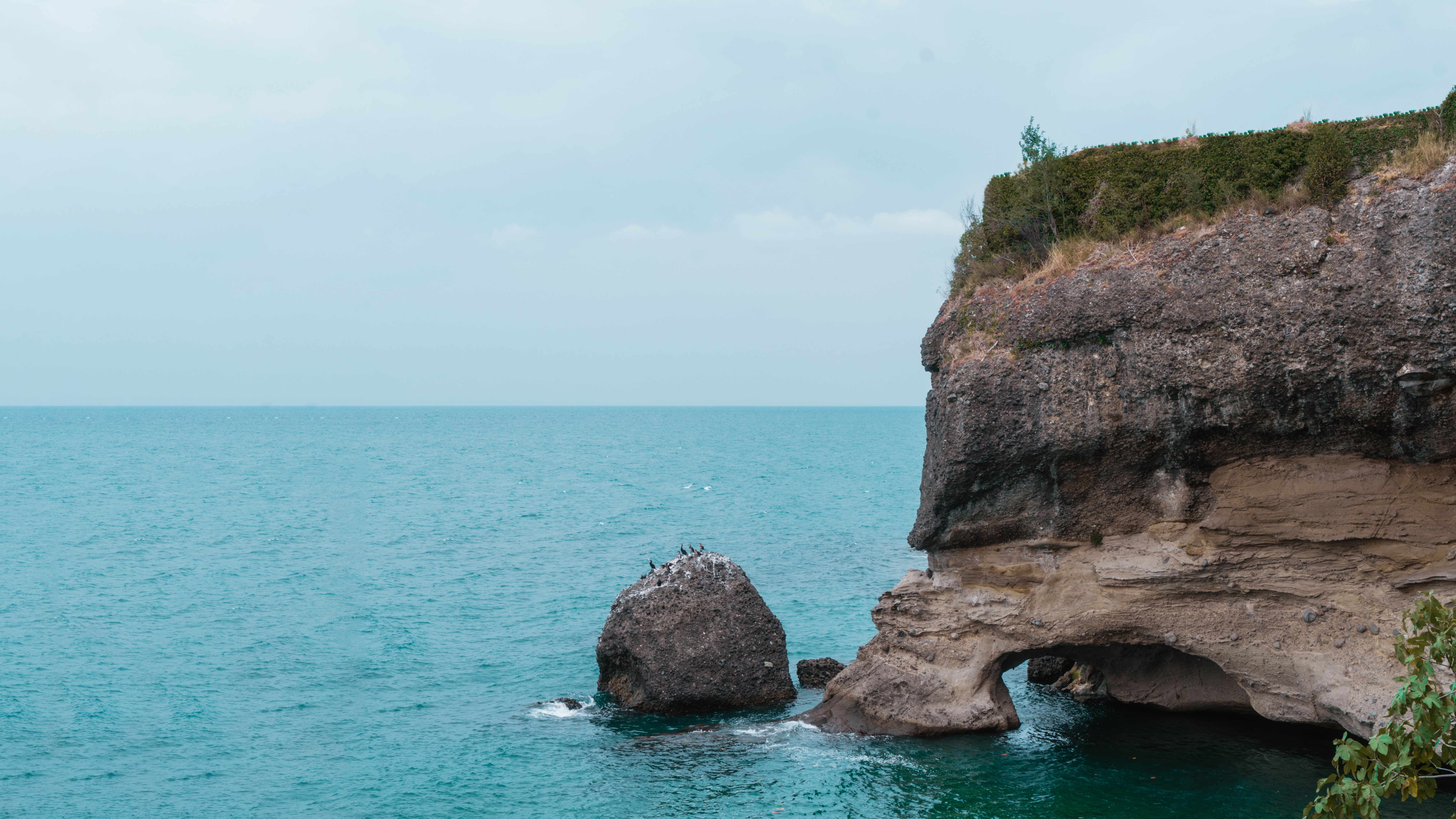 Turquoise water and rocky cliff with arch HD Wallpaper