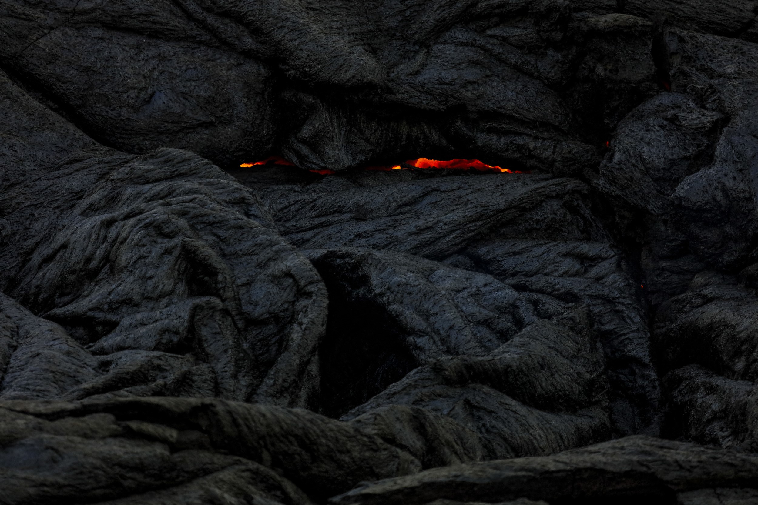 Molten lava glowing through dark volcanic rock formations HD Wallpaper