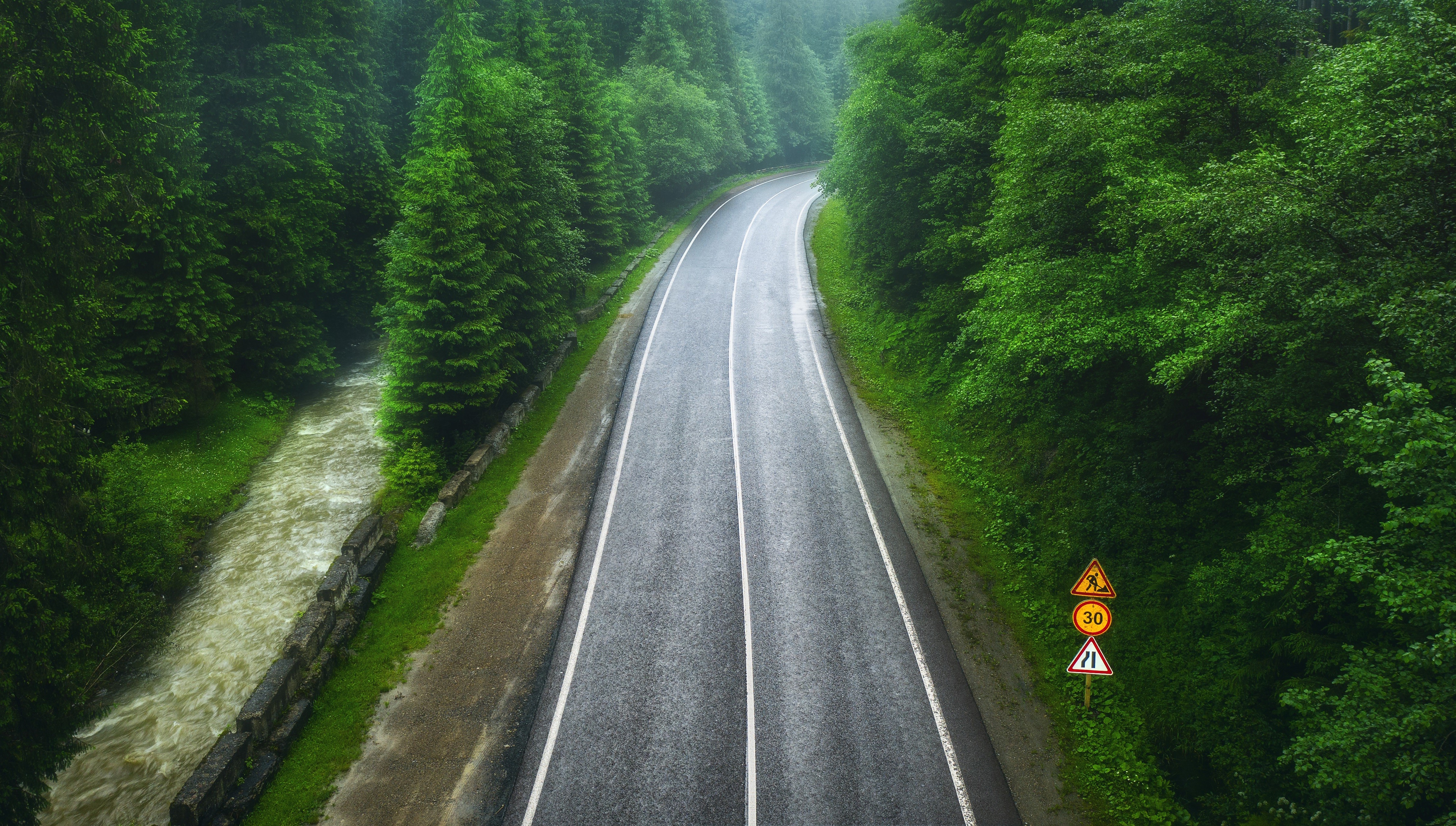 Aerial view of a winding road through a misty forest with a river HD Wallpaper