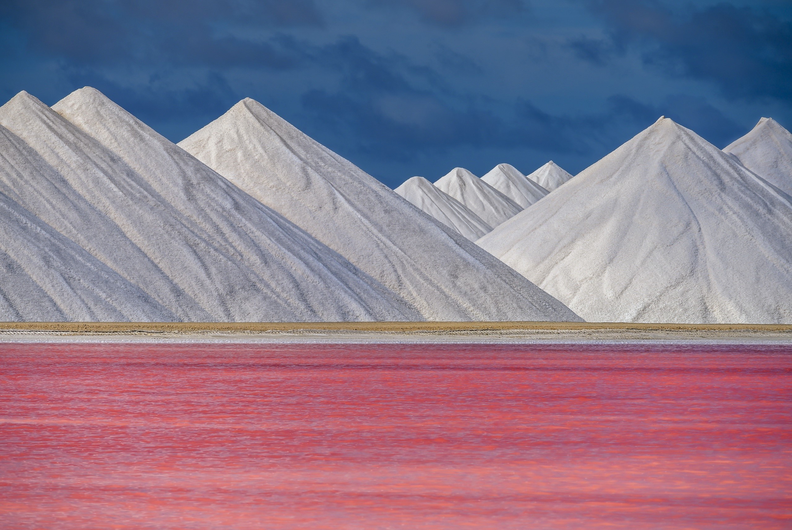 Salt piles by pink lake under dark clouds HD Wallpaper