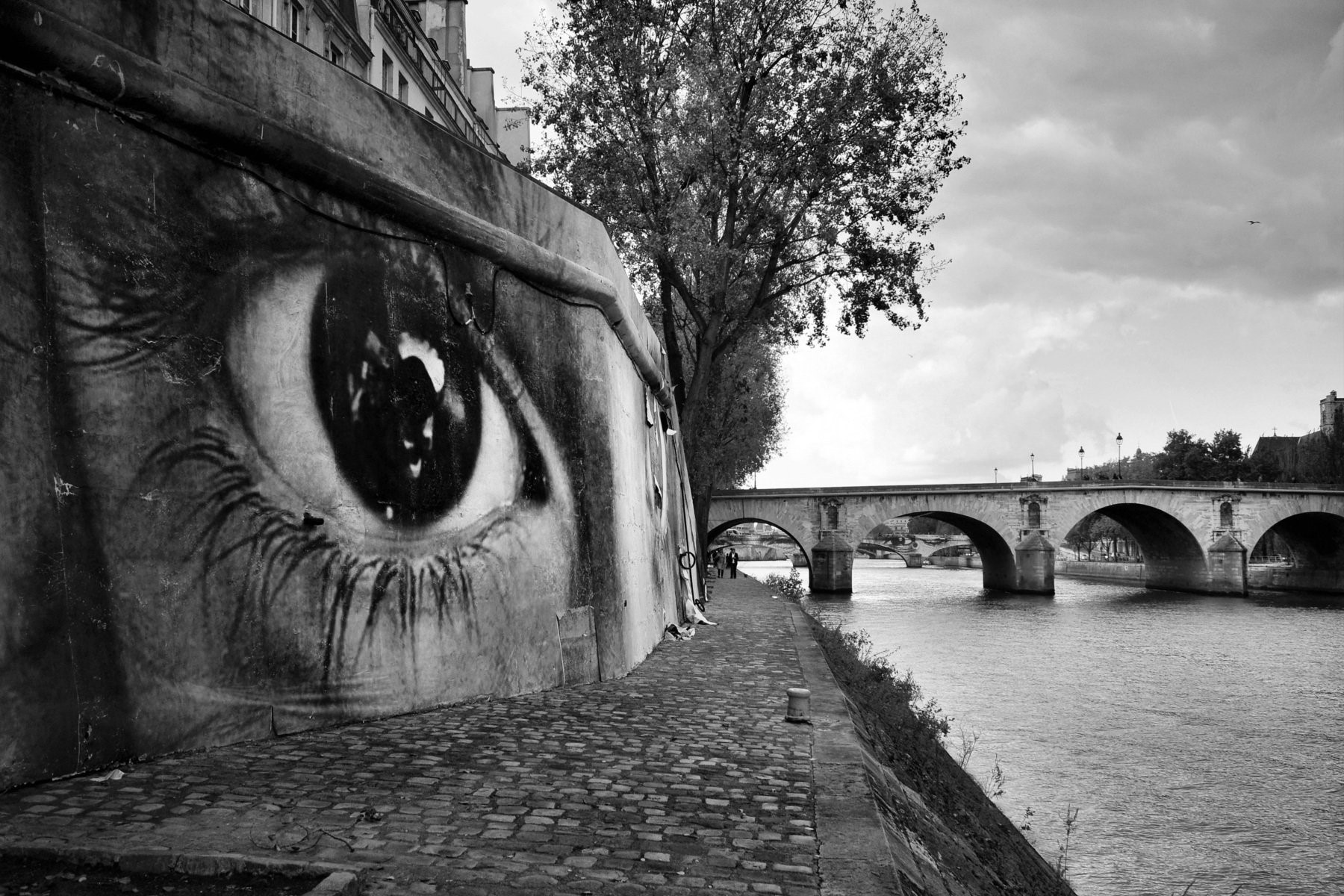 Giant eye mural on wall by river with bridge in Paris HD Wallpaper