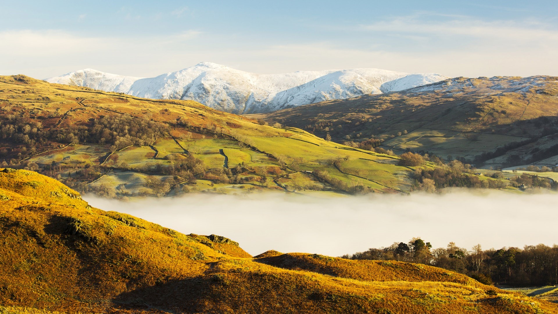 Snow-capped mountains over a misty valley and rolling hills HD Wallpaper
