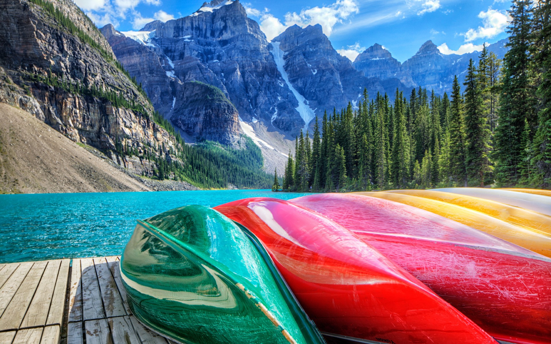 Colorful canoes on a wooden dock by a turquoise lake and mountains HD Wallpaper