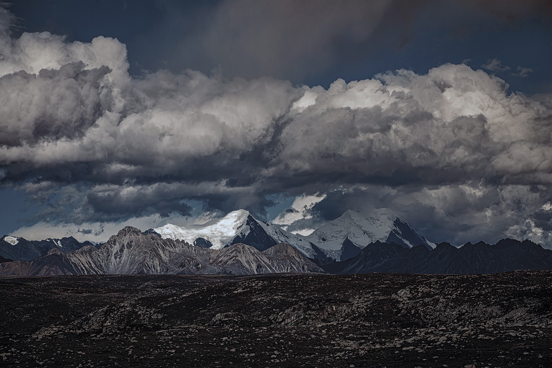 Dark clouds over snow-capped mountains and rocky foreground HD Wallpaper